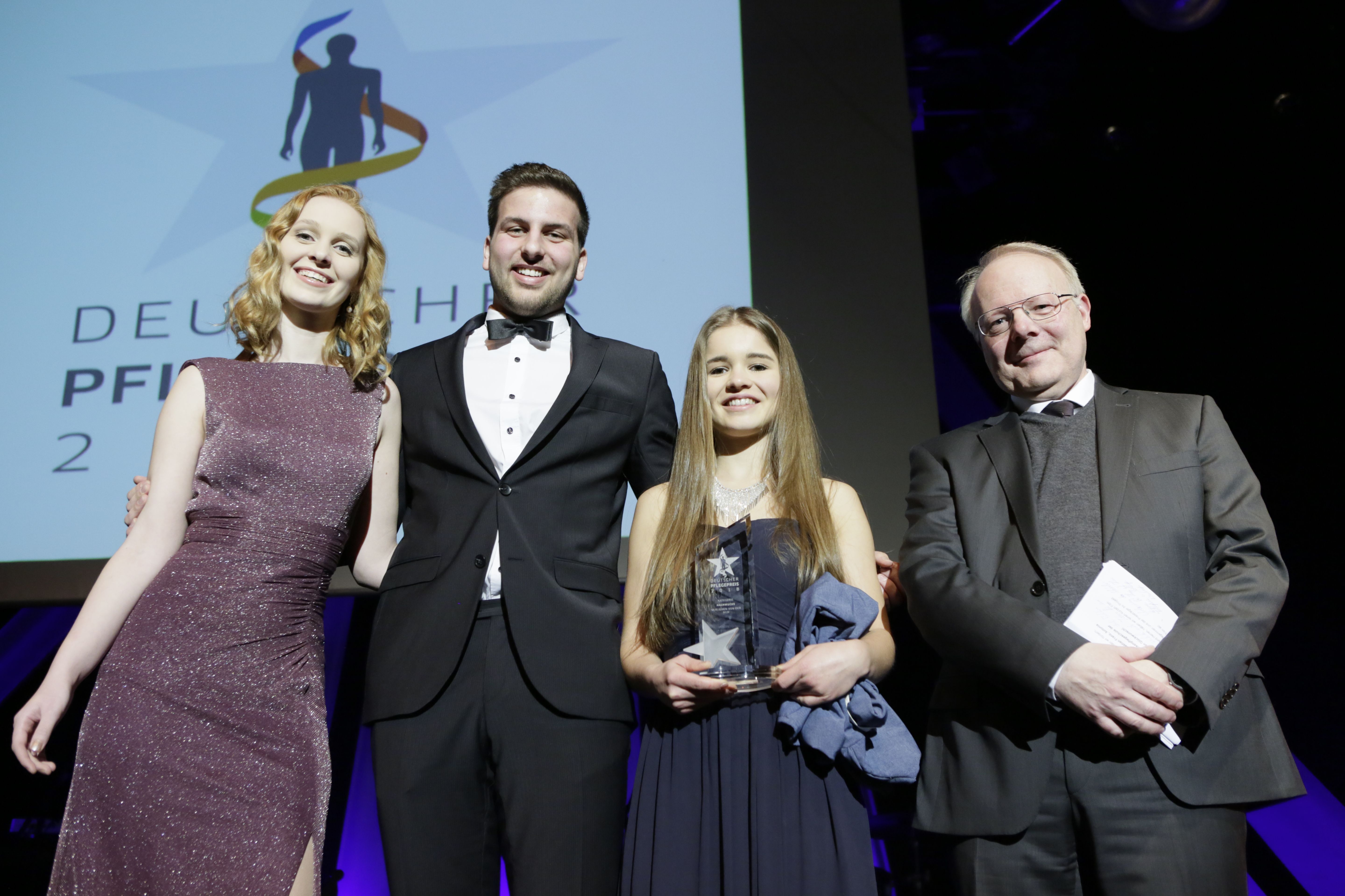 Die drei Gewinner und Gewinnerinnen des Nachwuchspreises 2018 zusammen mit dem Geschäftsführer der BGW auf einer Bühne auf dem Deutschen Pflegetag.