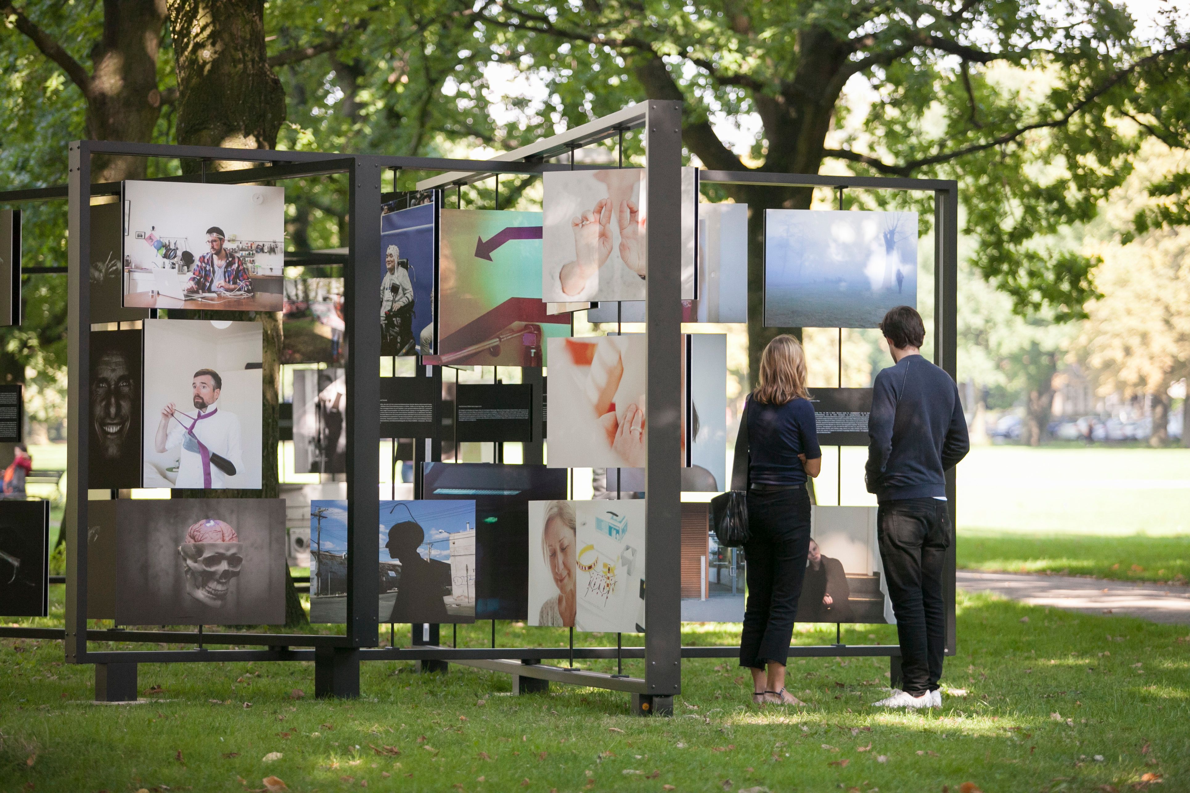 Zwei Personen auf einer Open-Air-Fotoausstellung, die auf großen drehbaren Tafeln präsentiert wird