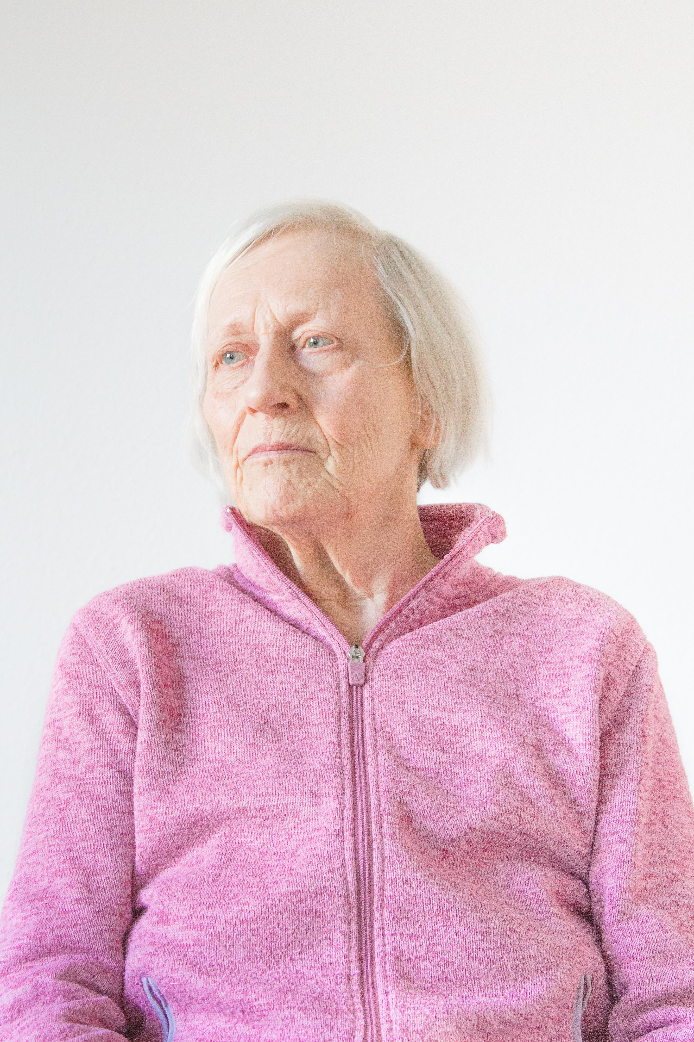 Eine ältere Frau in einem pinken Pullover. Sie schaut an der Kamera vorbei.