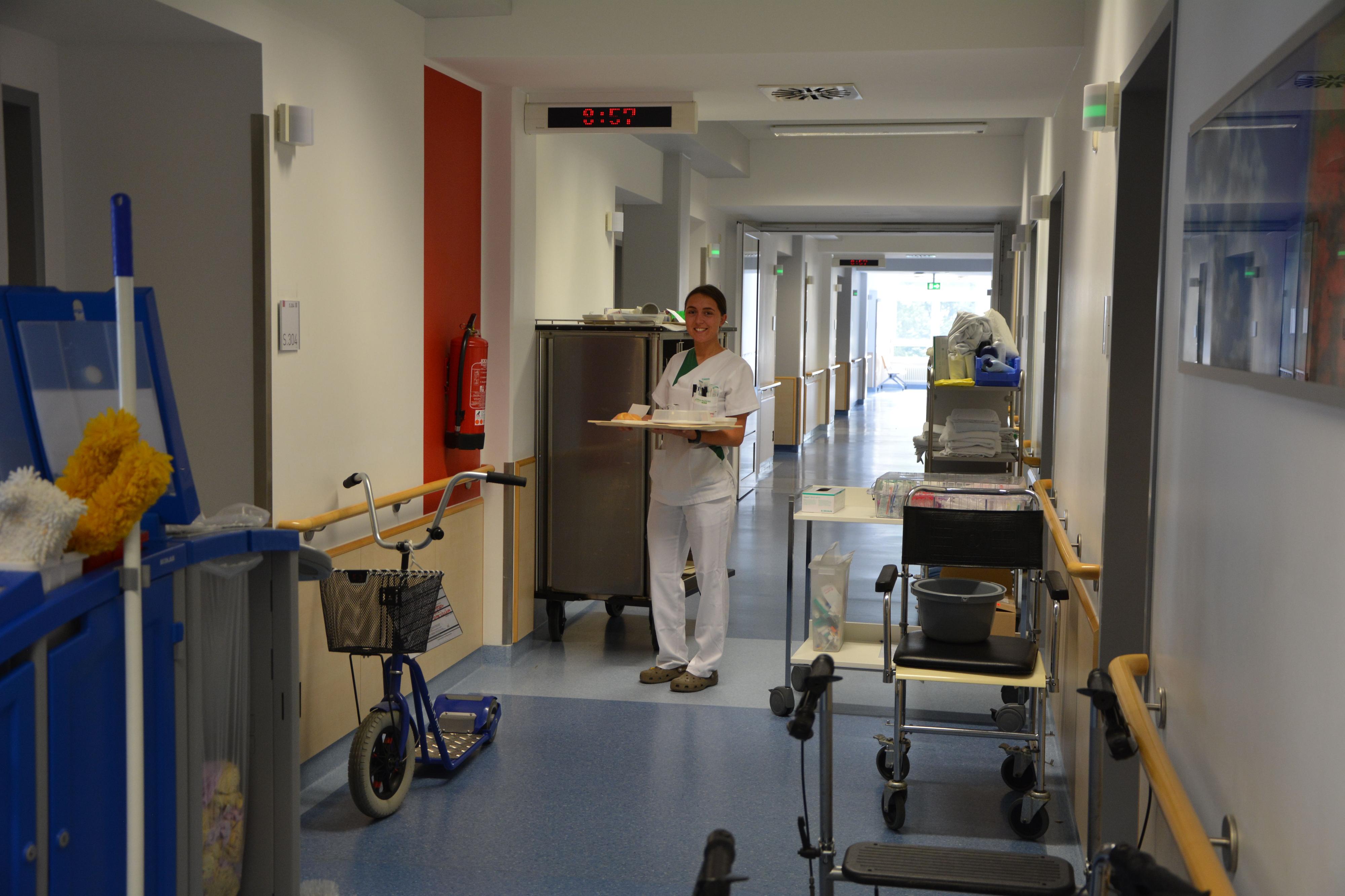 Eine Pflegerin steht mit einem Tablett in einem Krankenhausflur.