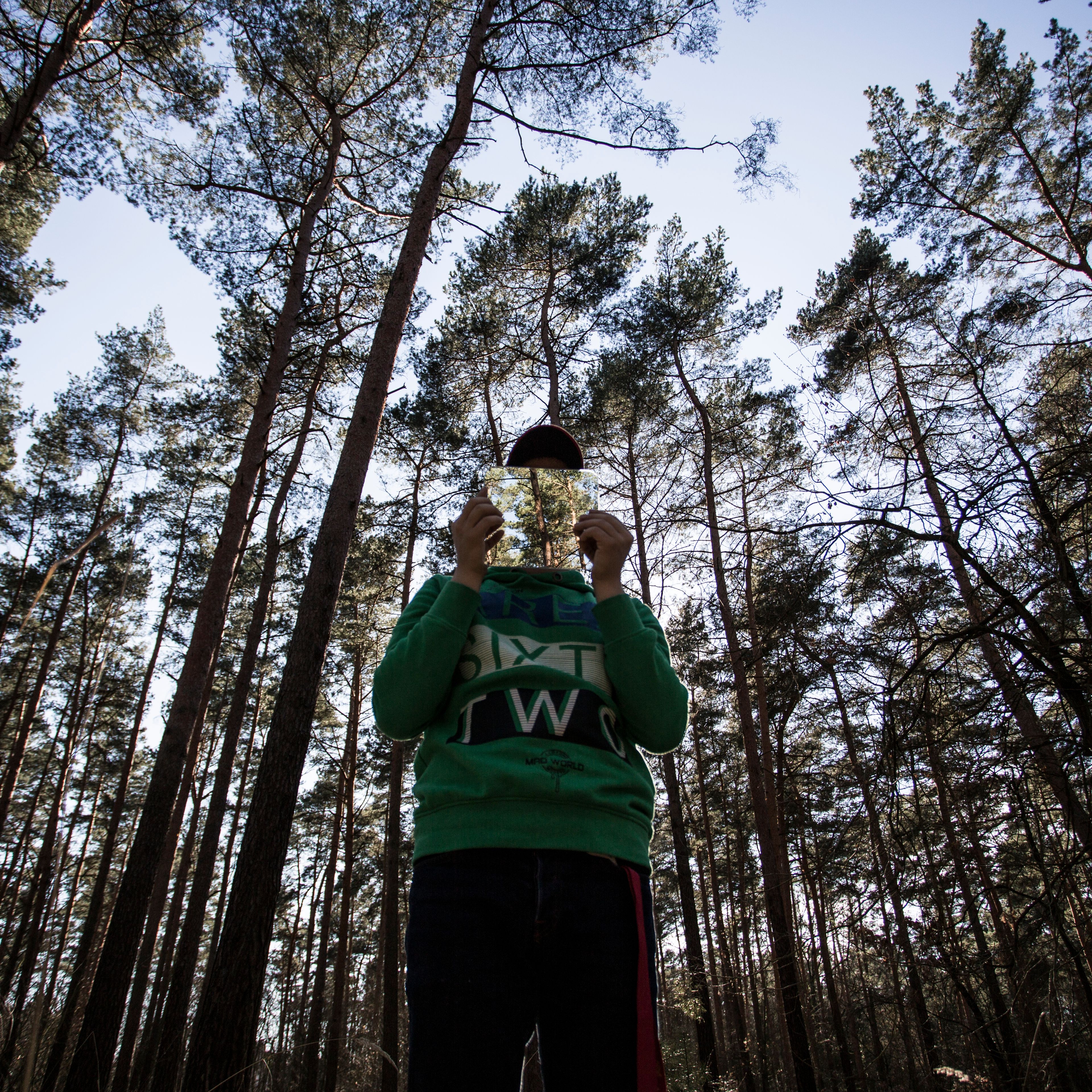 Ein Mann steht im Wald und hält ein Foto eines Waldes vor sein Gesicht.