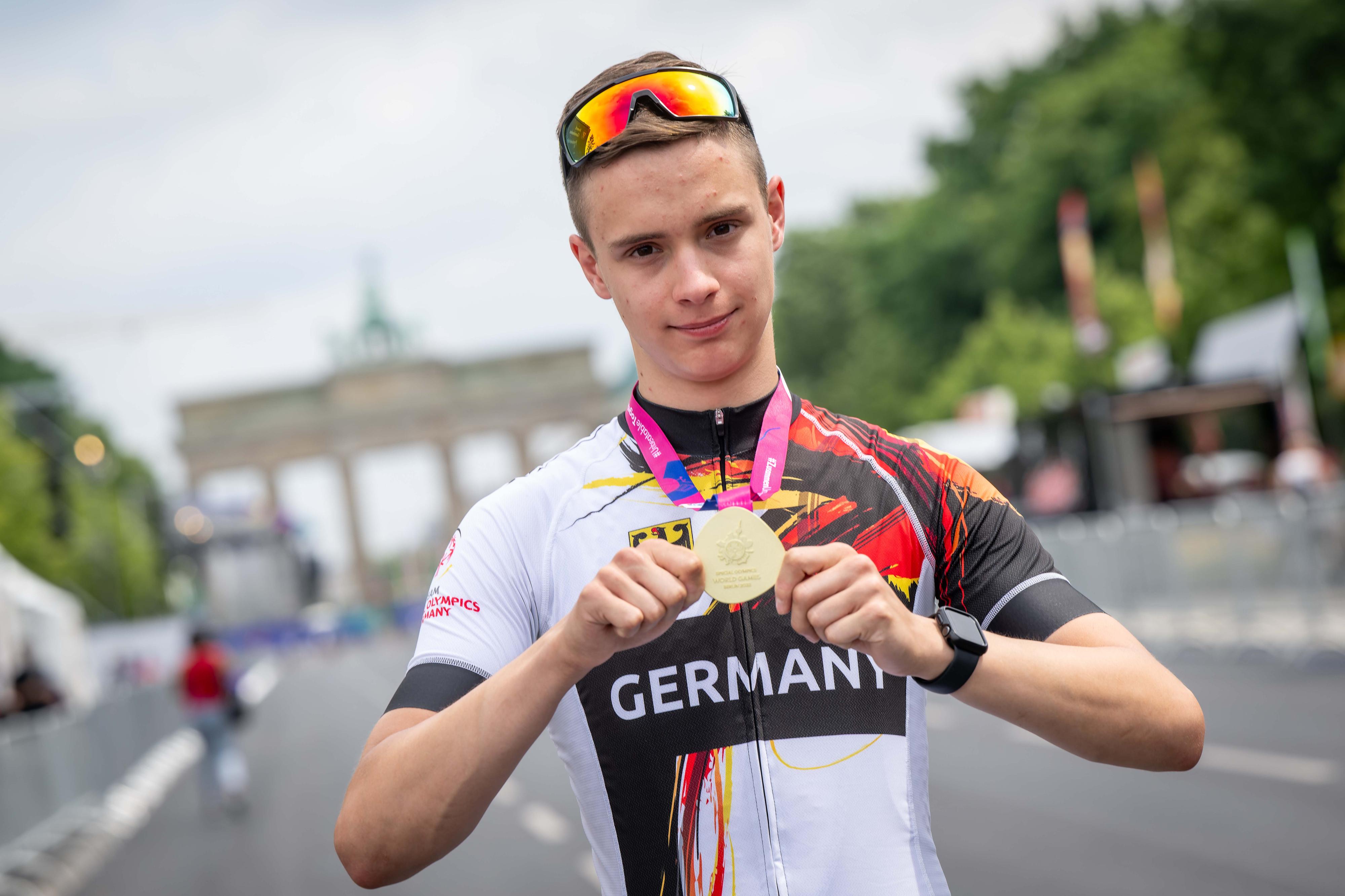 Leon Colberg hält mit beiden Händen seine Goldmedaille in die Kamera. Im Hintergrund das Brandenburger Tor.