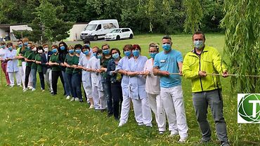 Mitarbeitende der Tannenhofer Fachpflegeheime GmbH stehen in einer Reihe und ziehen zusammen an einem langen Seil. Alle tragen medizinische Masken.