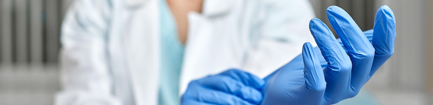 Eine Ärztin zieht blaue Latexhandschuhe an.