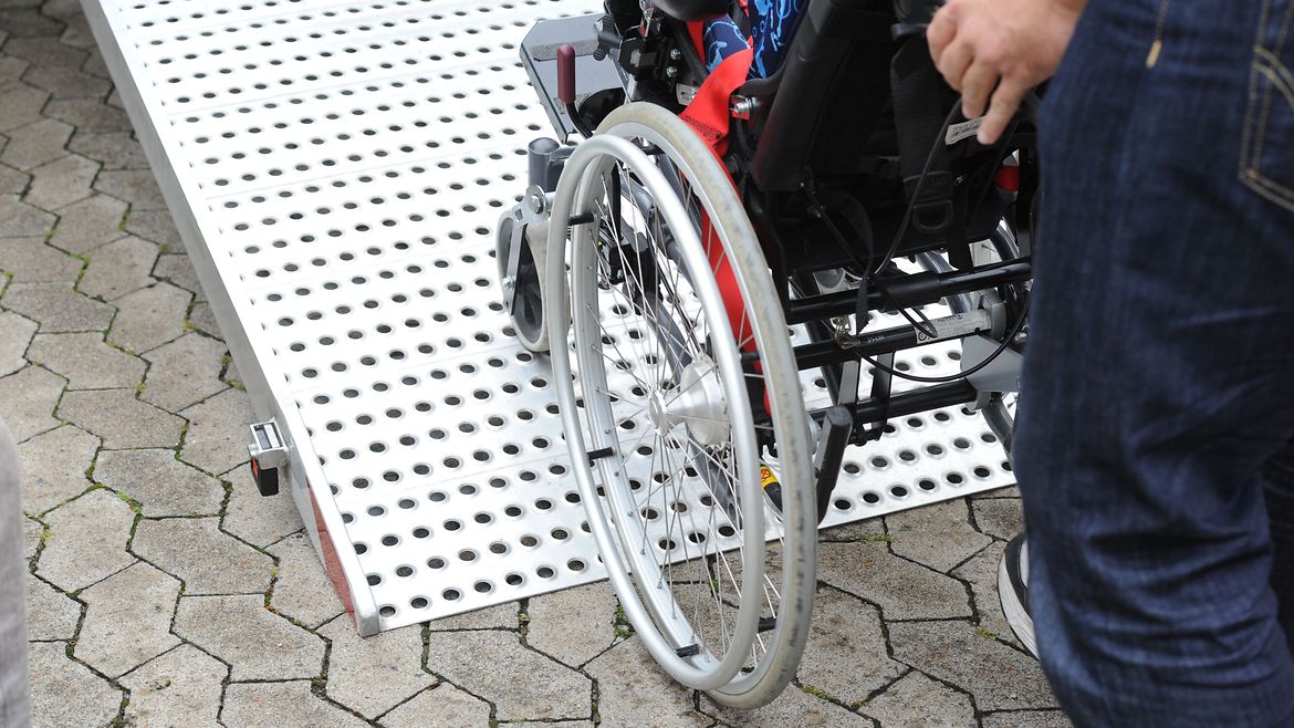 Rollstuhl wird über eine Metallrampe in ein Fahrzeug geschoben.