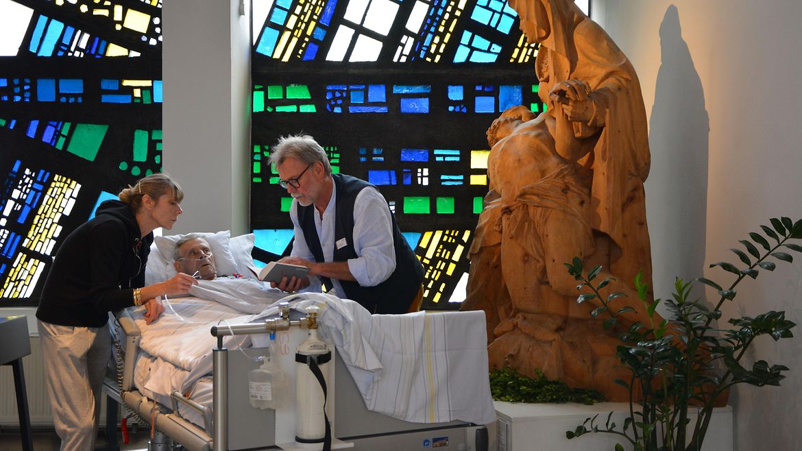 Ein älterer Mann liegt in einem Krankenbett in einer Kirche.