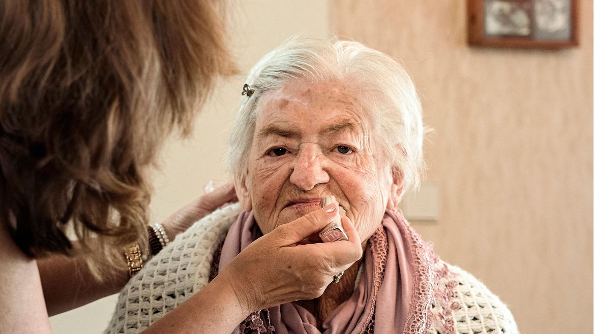 Eine Frau trägt einer älteren Frau Lippenstift auf.