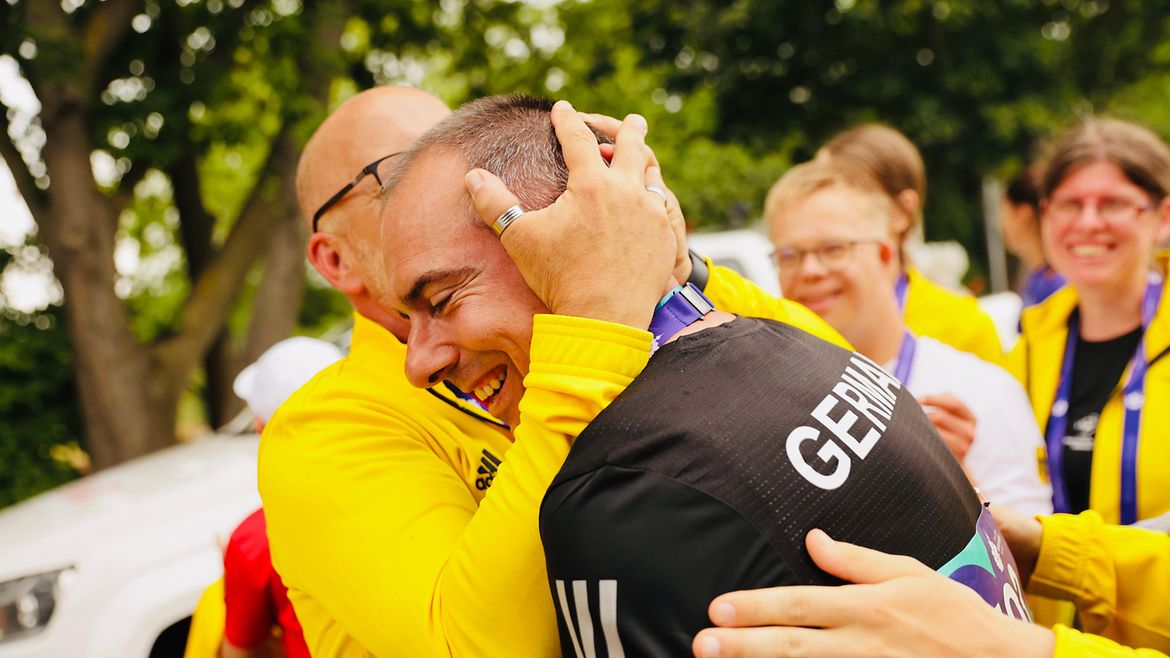 Marco Fähling wird umarmt von einem Mann, der ihn zusich heranzieht. Im Hintergrund freudige Gesichter