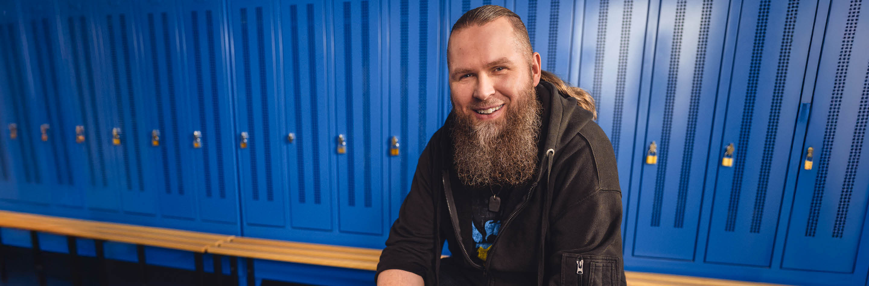 1000 UNDEIN GRUND – Deine Idee von Karriere: mehr bewirken. Ein Mann mit langem Bart sitzt auf einem Gymnastikball in einer Umkleidekabine
