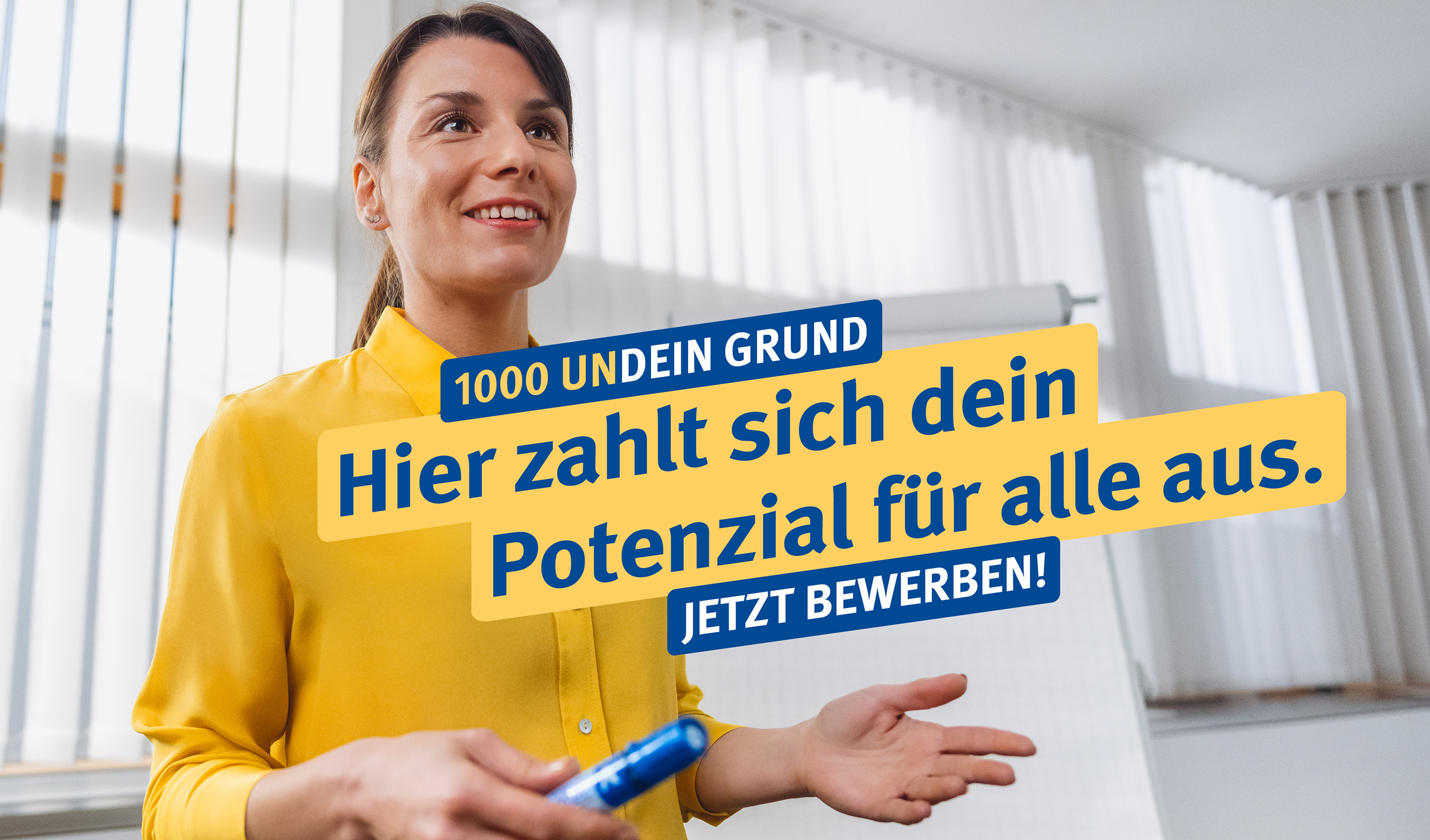 1000UNDEIN GRUND Eine junge Frau in einer gelben Bluse steht vor einem Flipchart im Büro.