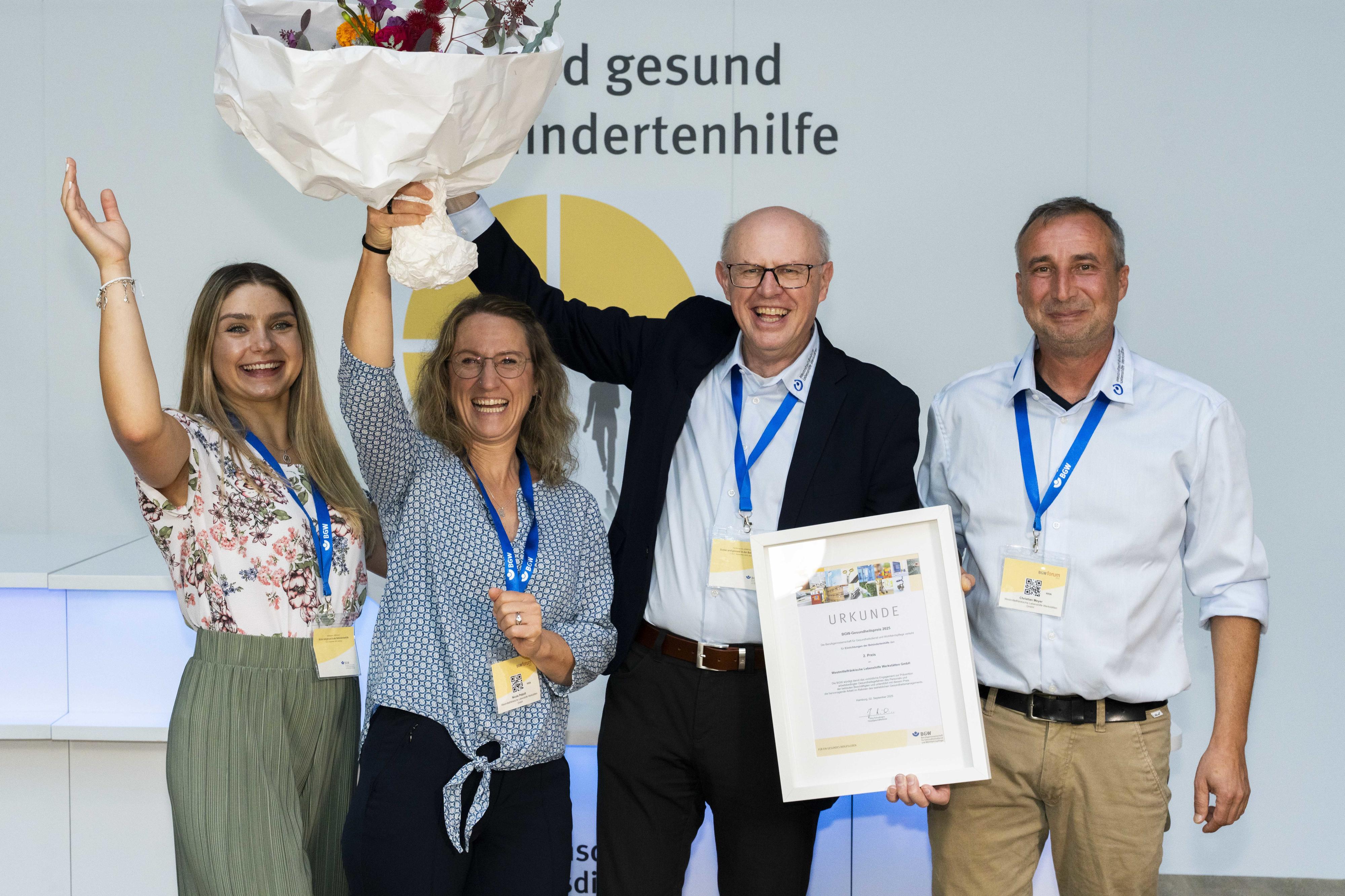 Vier jubelnde Personen, zwei davon halten einen Blumenstrauß in die Höhe.