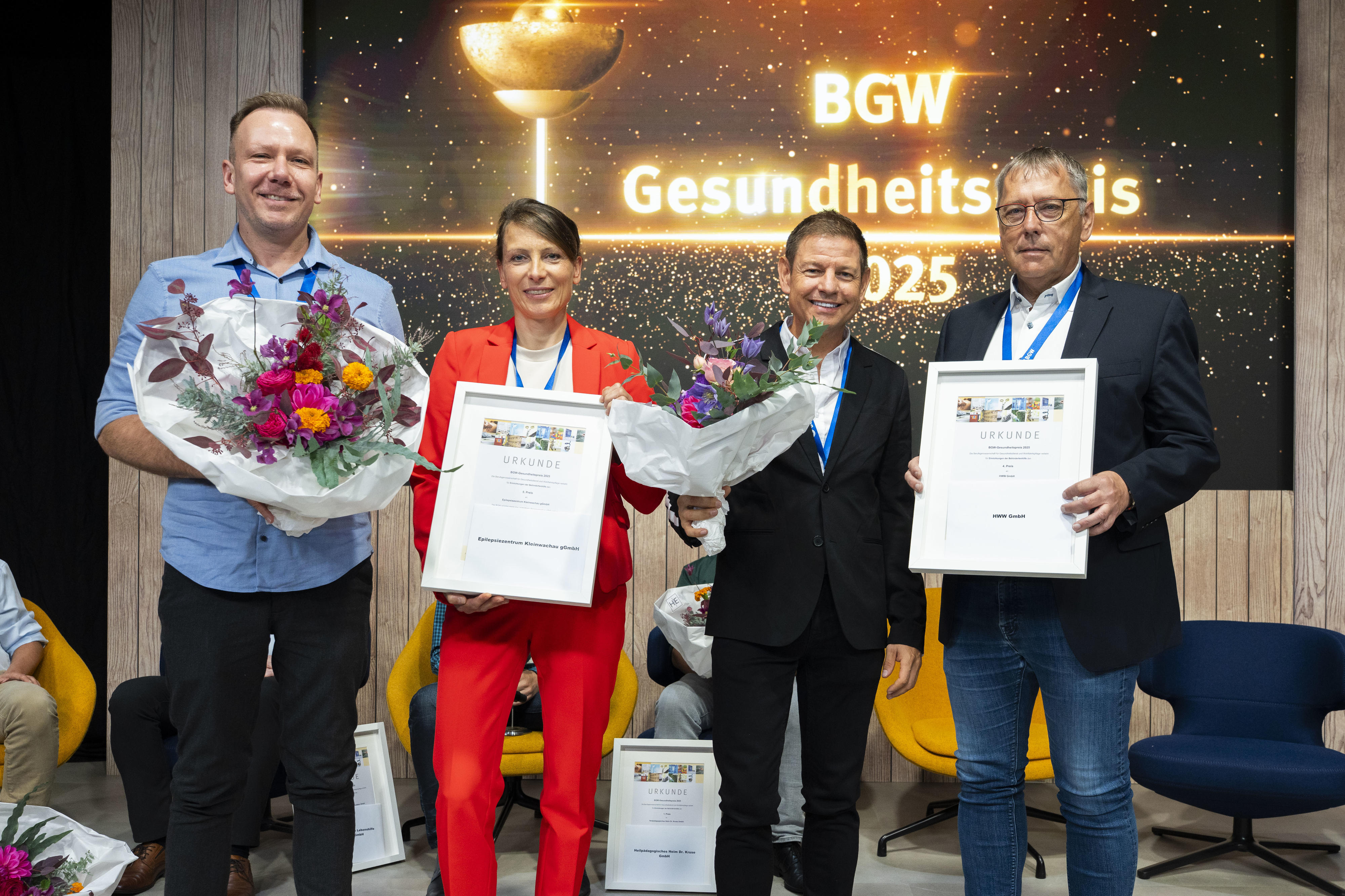 Vier Personen, zwei Personen halten jeweils einen Blumenstrauß, zwei Personen jeweils eine Urkunde