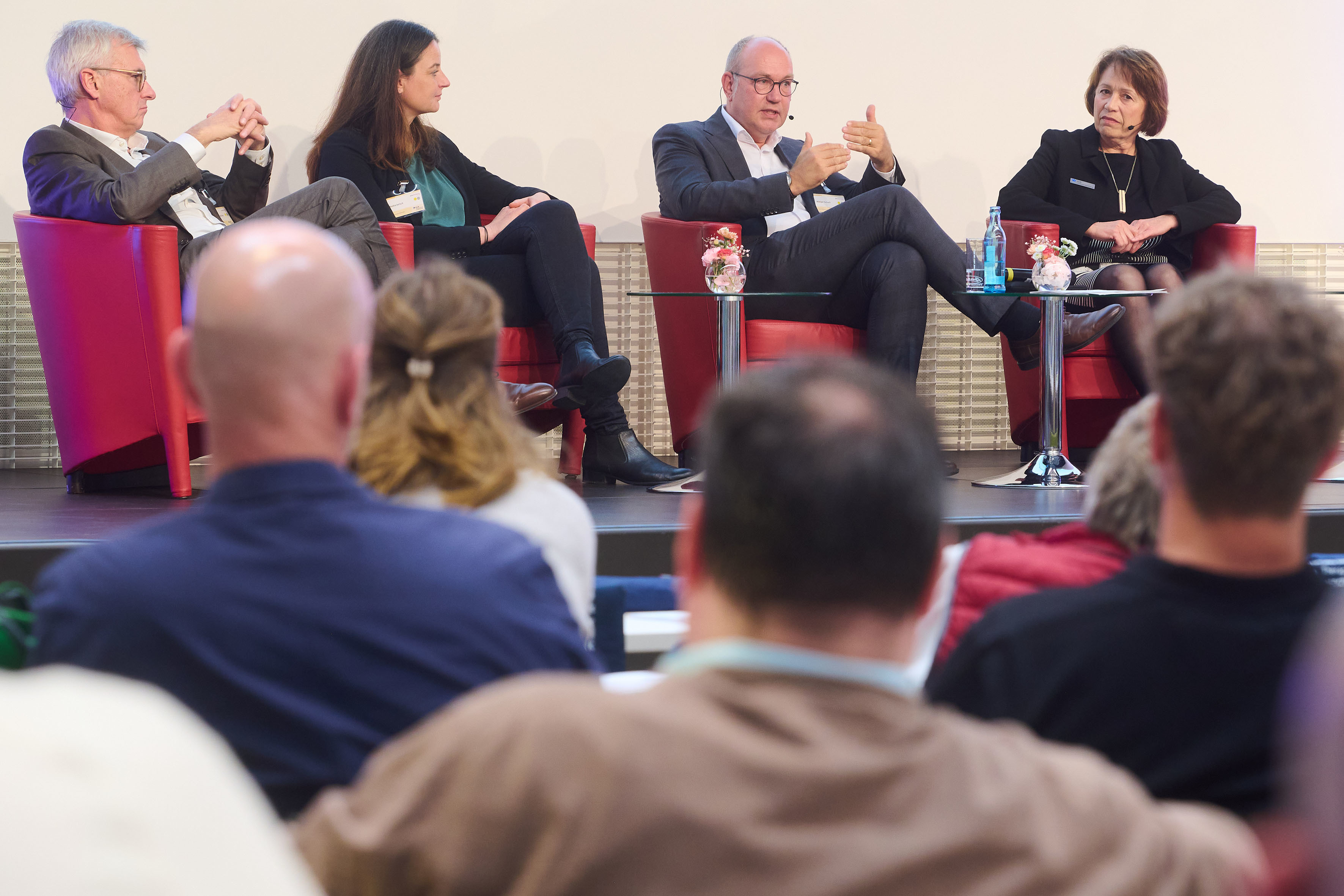 Blick aus dem Publikum auf eine Bühne, auf der zwei Mäönner und zwei Frauen in Sesseln sitzen und diskutieren.