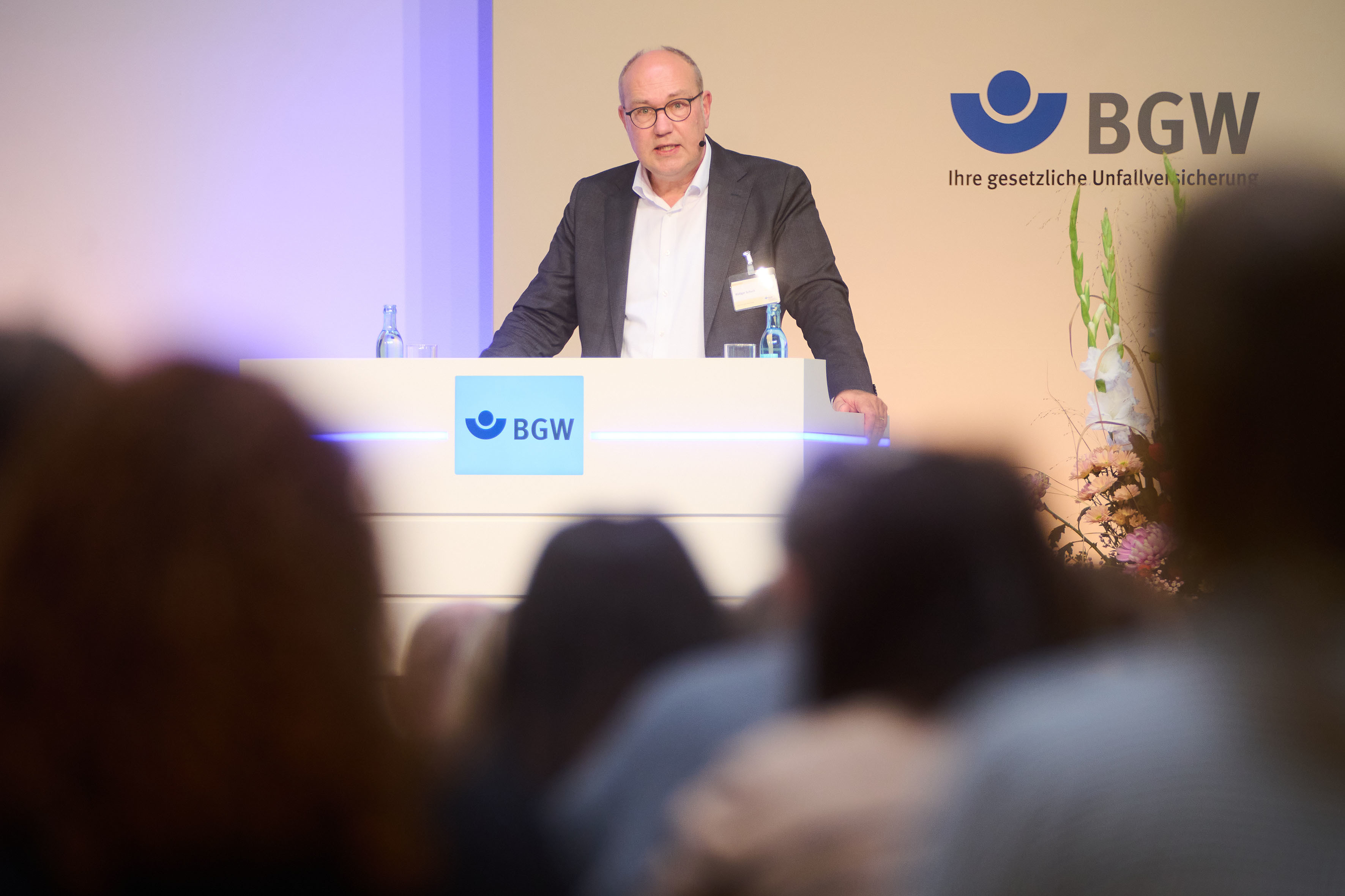 Blick aus dem Publikum zu einem Podium, an dem Rüdiger Schuch, Präsident der Diakonie Deutschland, steht und spricht.