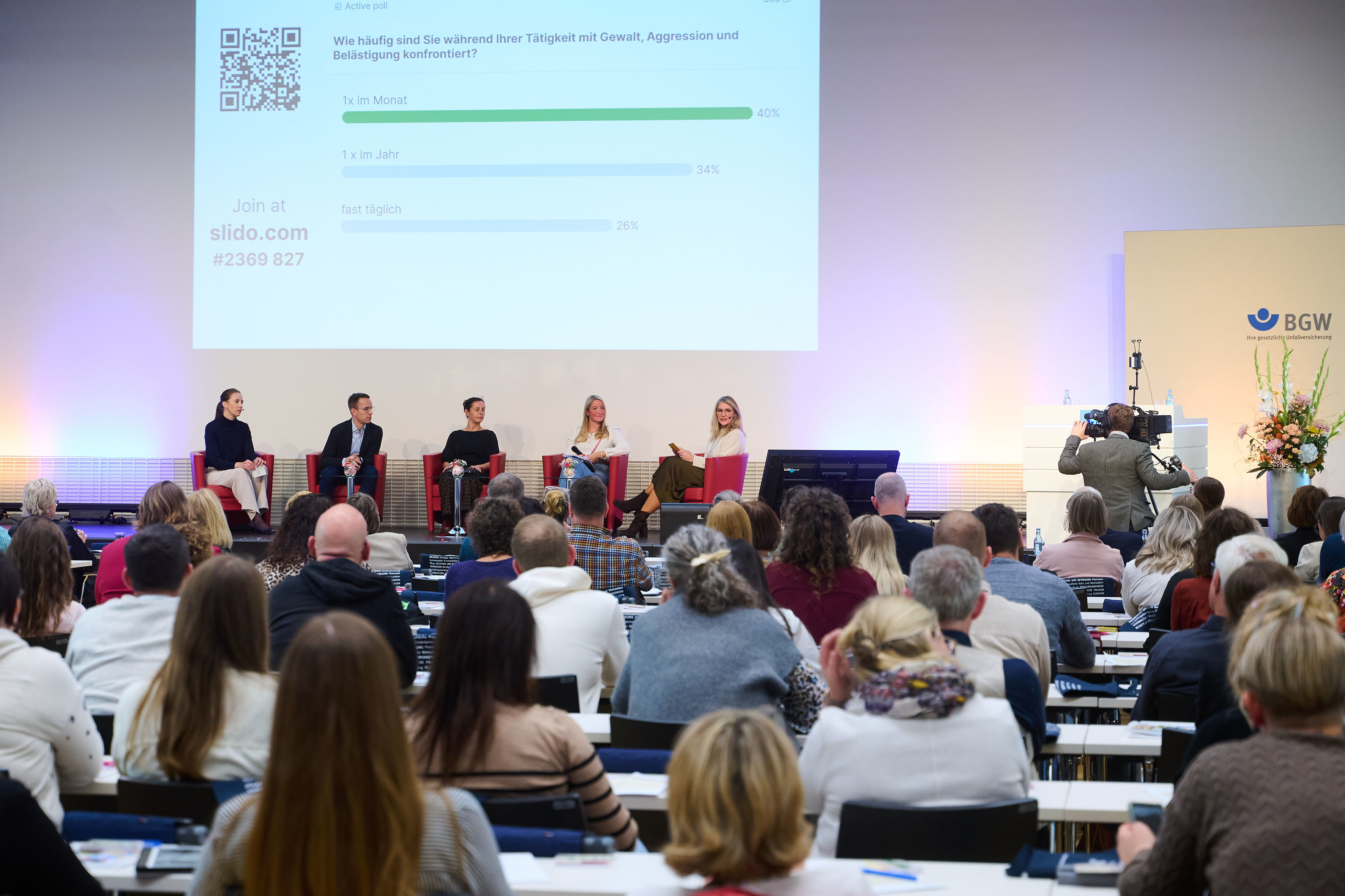 Blick aus dem Publikum auf eine Bühne, auf der vier Frauen und ein Mann auf Stühlen sitzen und dikutieren.