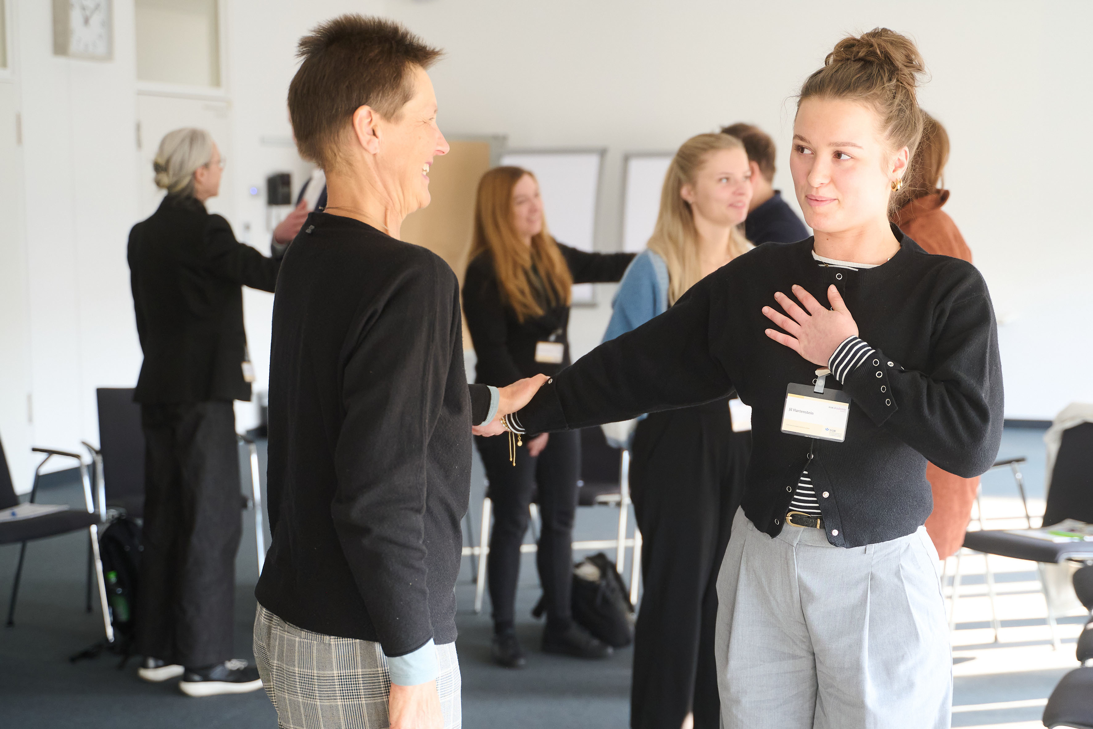 Zwei Frauen stehen sich bei einem Workshop gegenüber und halten sich am Arm fest, eine Frau hält die Hand auf ihre Brust.