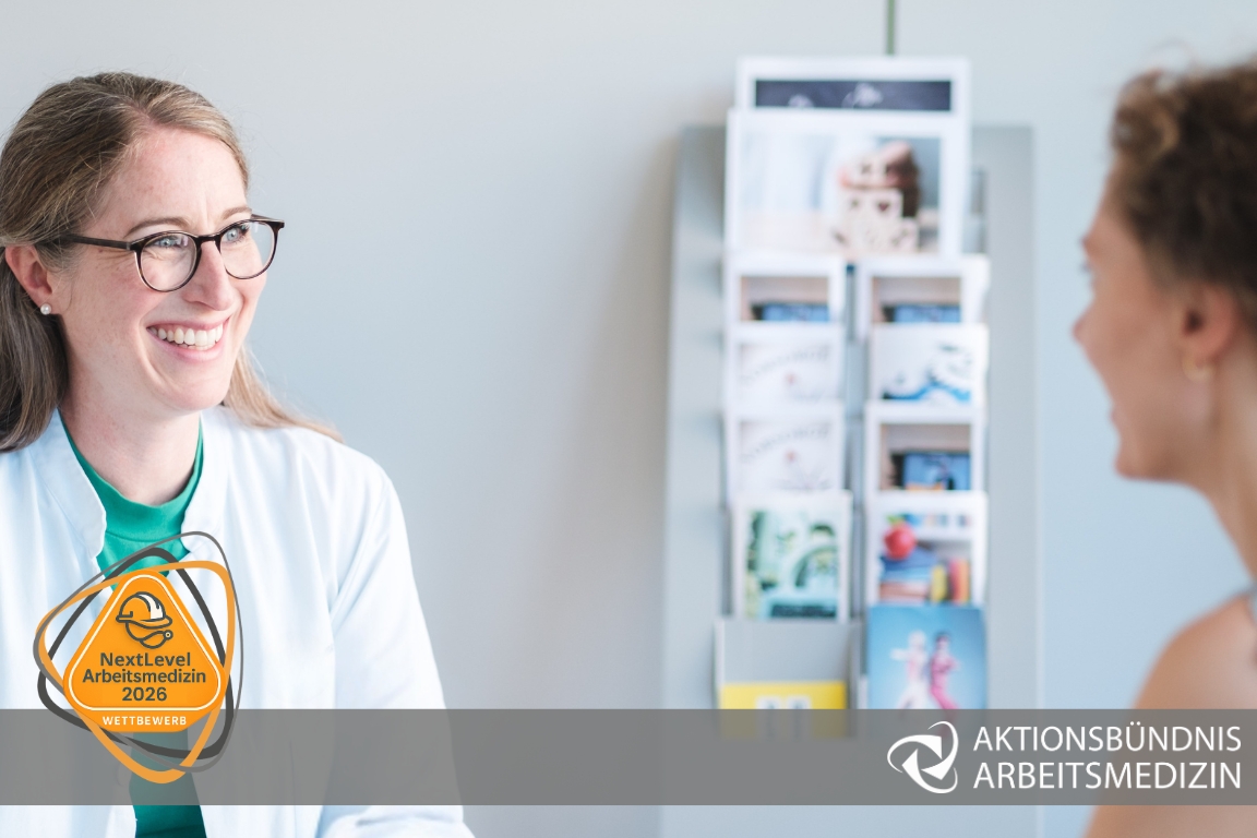 Eine Frau im weißen Kittel im Gespräch mit einer anderen Frau mit Störer NextLevel Arbeitsmedizin 2025 Wettbewerb