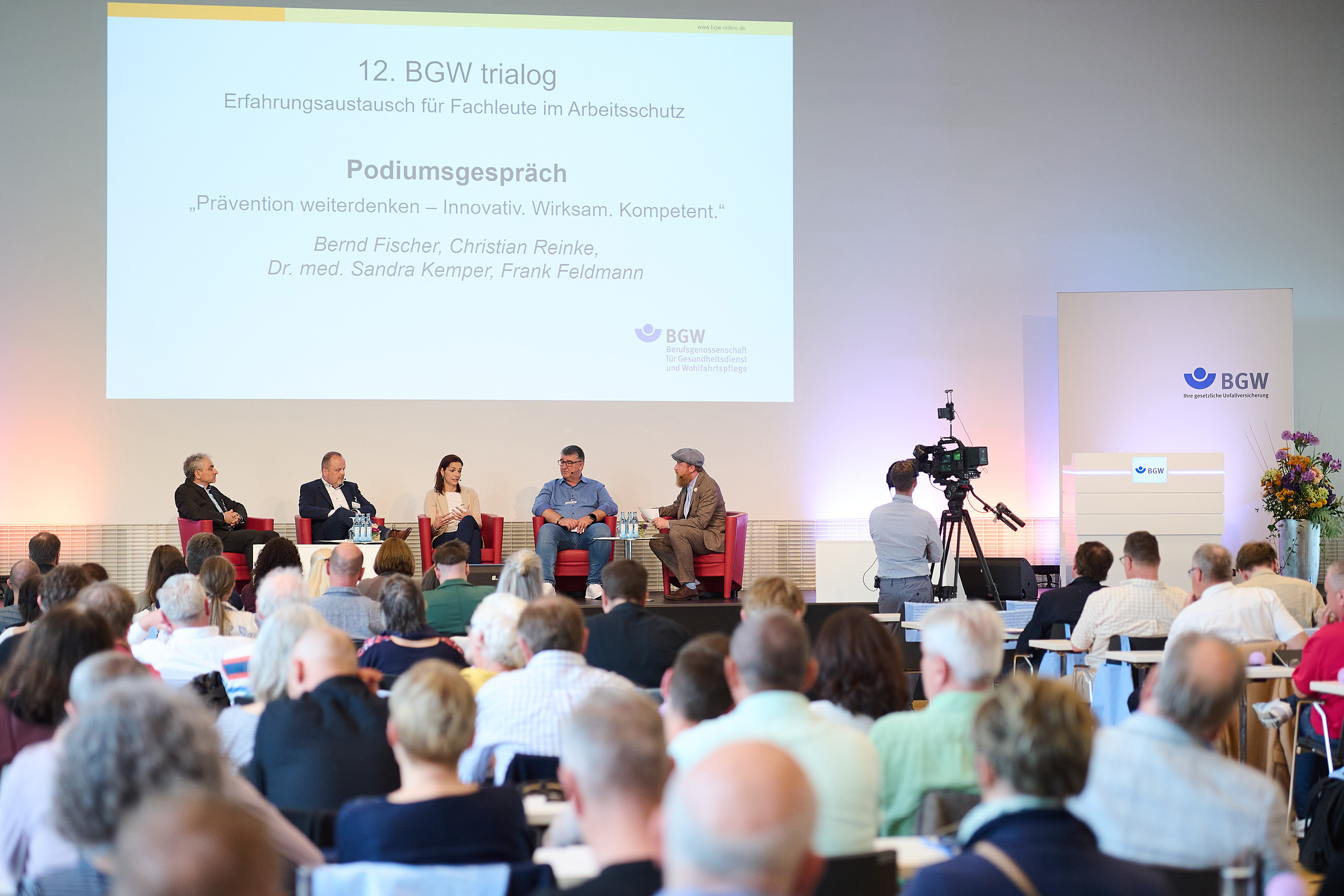 Blick aus dem Publikum auf die Bühne des trialogs: Fünf Personen sitzen in Stühlen zu einem Podiumsgespräch zusammen.