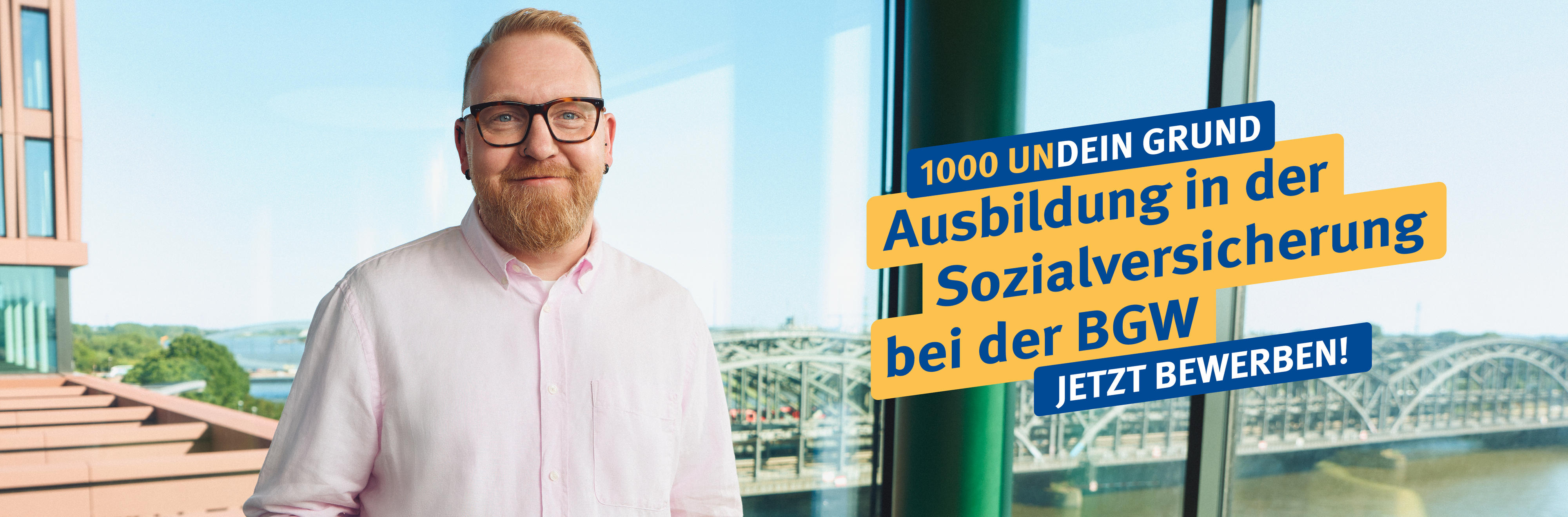 Ein Mann mit Brille und Vollbart lächelt in die Kamera, hinter ihm sieht man durch die Fensterfront die Hamburger Elbbrücken. Daneben Schrift: 1000 Undein Grund – Ausbildung in der Sozialversicherung bei der BGW – Jetzt bewerben!