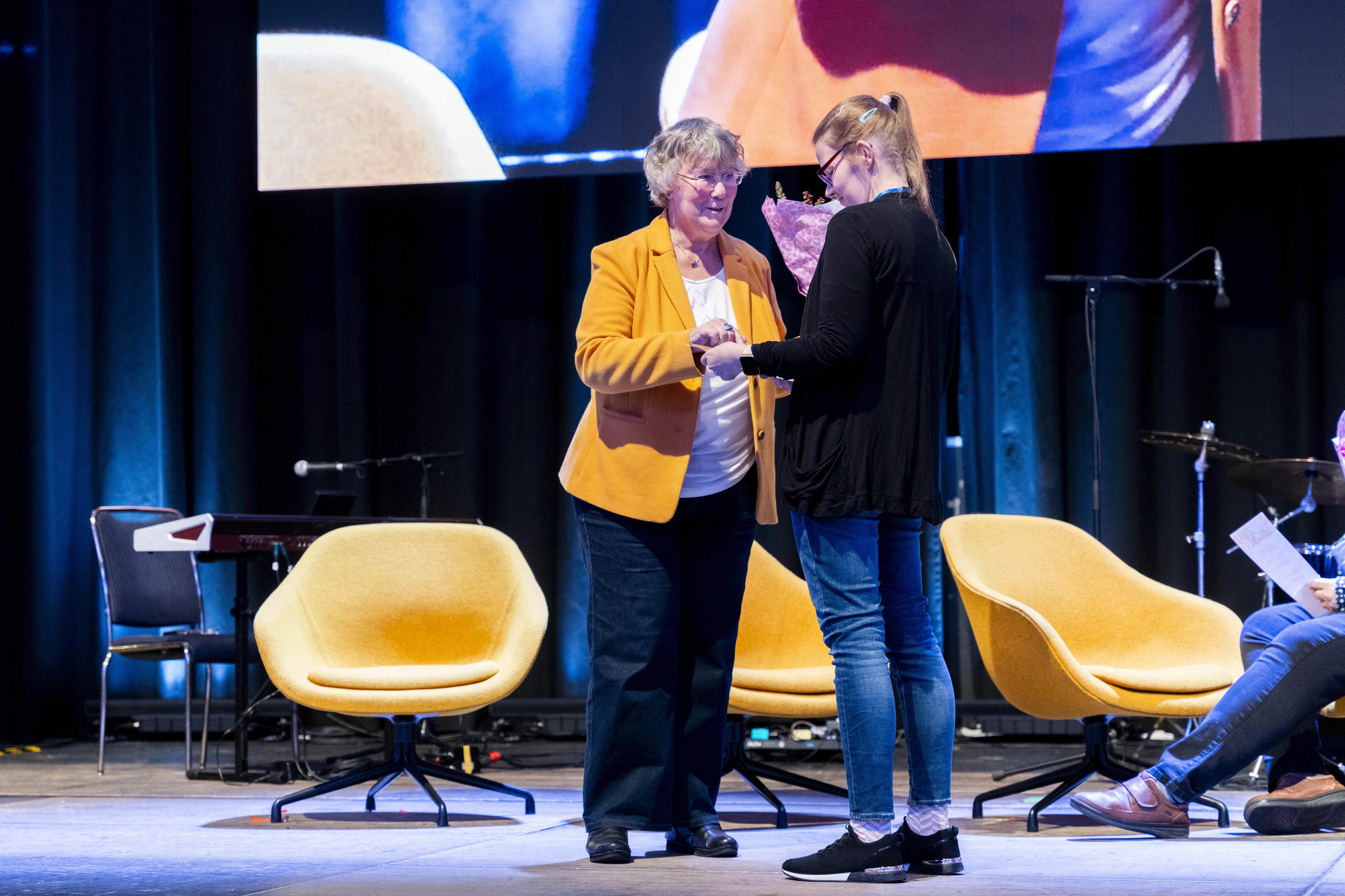 Silvia Thimm (l.) aus der BGW Selbstverwaltung mit der Gewinnerin des 2. Platzes Jaqueline Schwiderski auf einer Bühne.