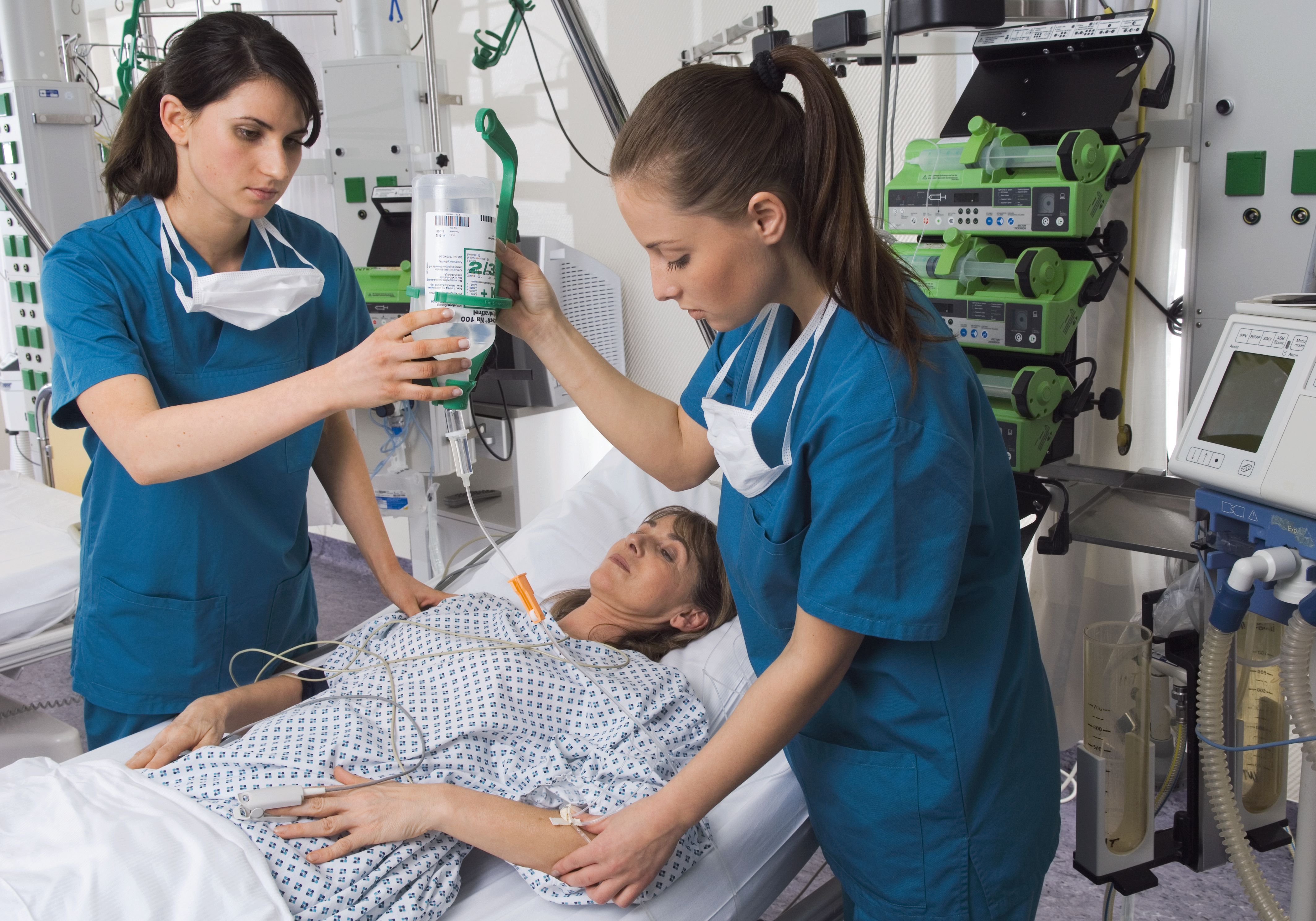 Zwei Krankenpflegerinnen legen eine Infusion bei einer Patientin.