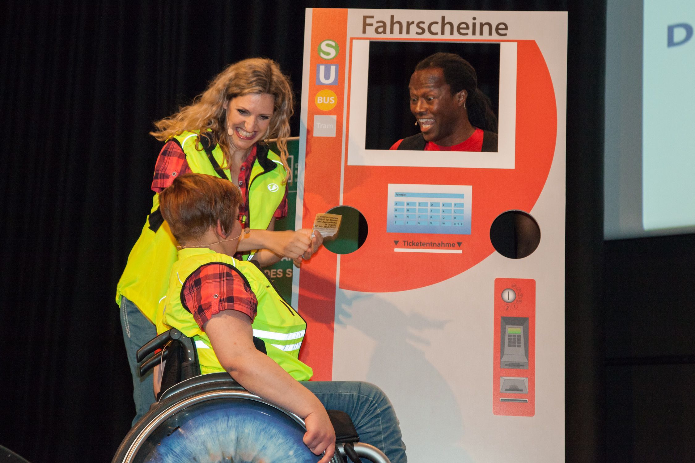 Aus der Kompetent mobil Show: Akteurin zeigt Rollstuhlnutzerin die Bedienung eines Fahrkartenautomaten