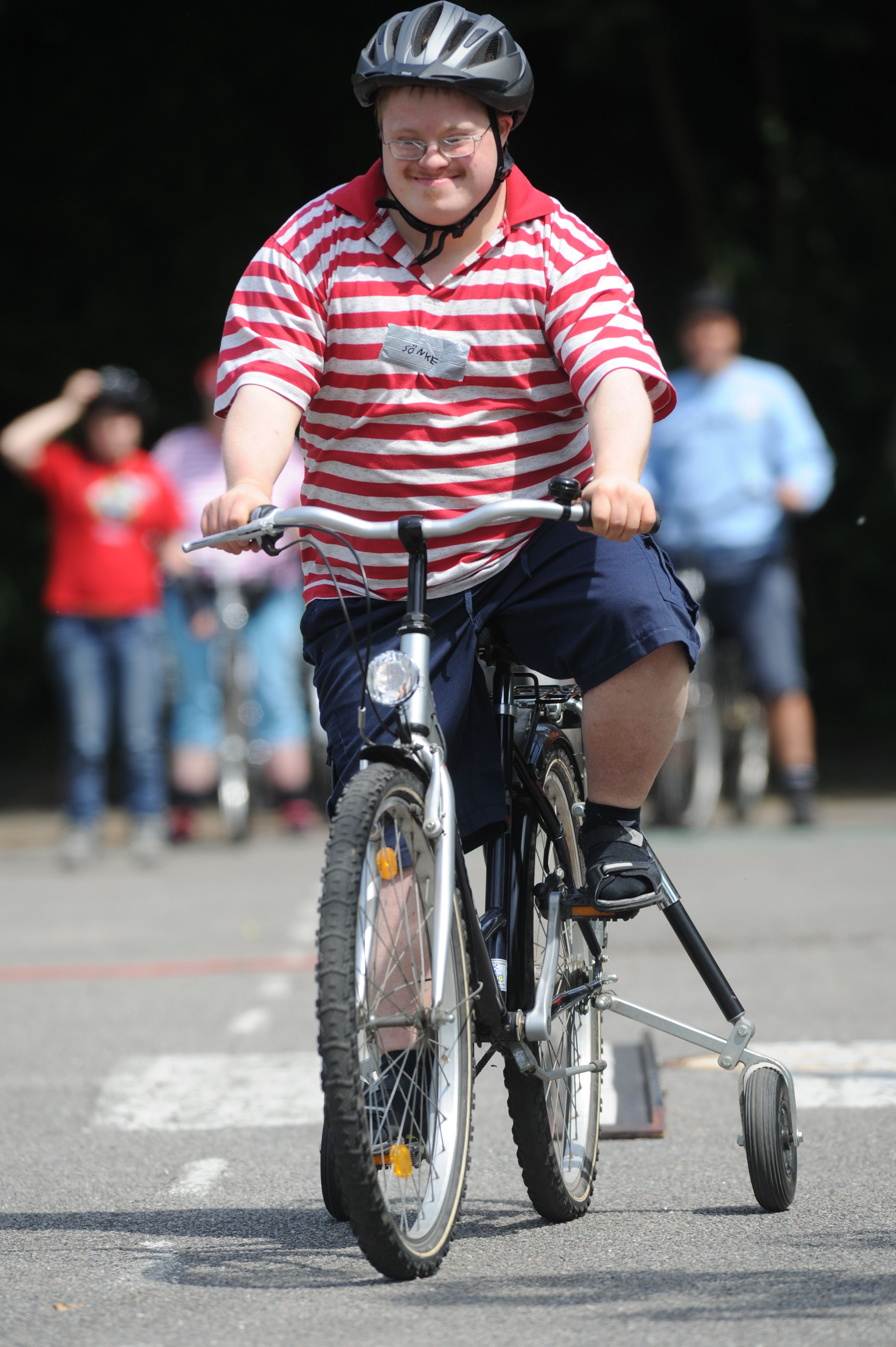 Mensch mit Behinderung fährt auf einem Fahrrad mit Stützrädern.