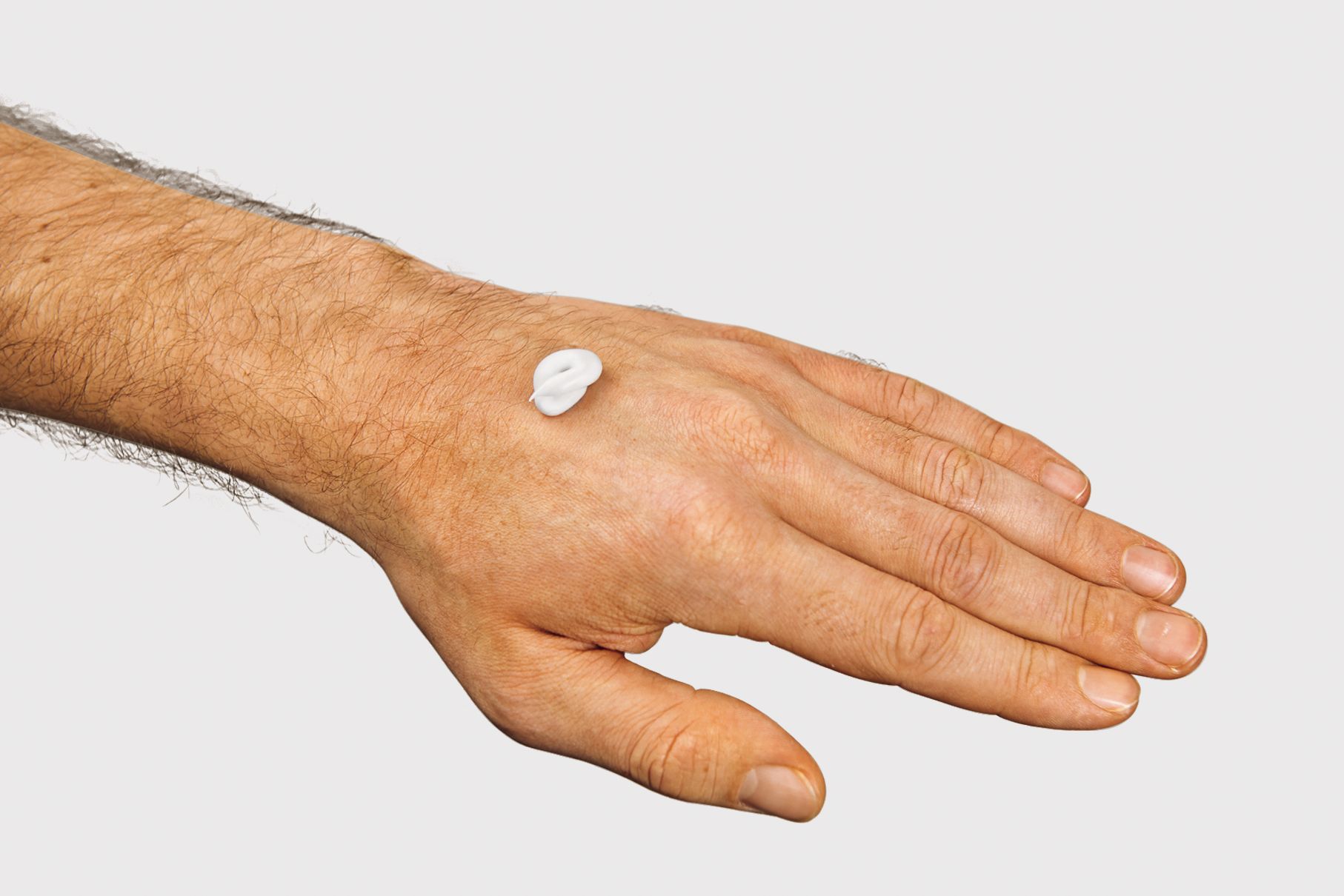 Einen etwa haselnussgroßen Klecks Creme auf dem Handrücken einer Männerhand.