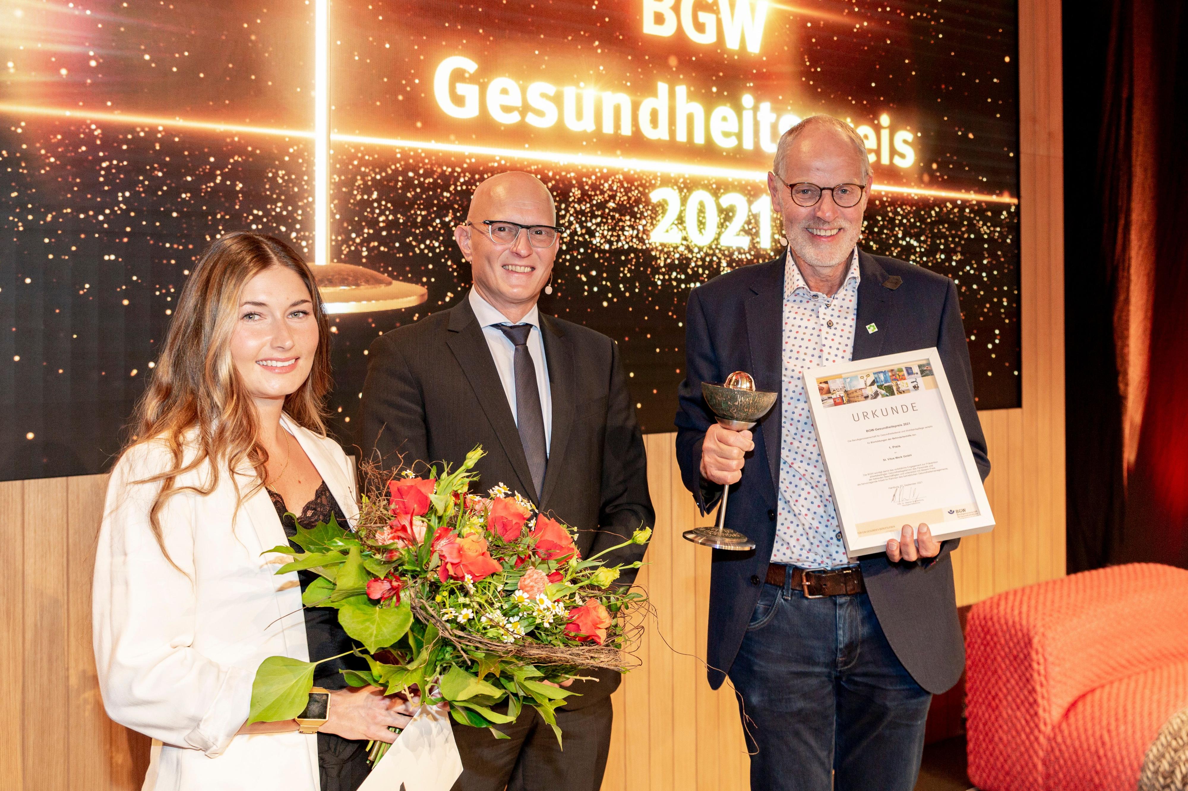 Rebecca Schmuda-Besancon mit Blumenstrauß, Jörg Schudmann und Johannes Münzebrock mit Urkunde