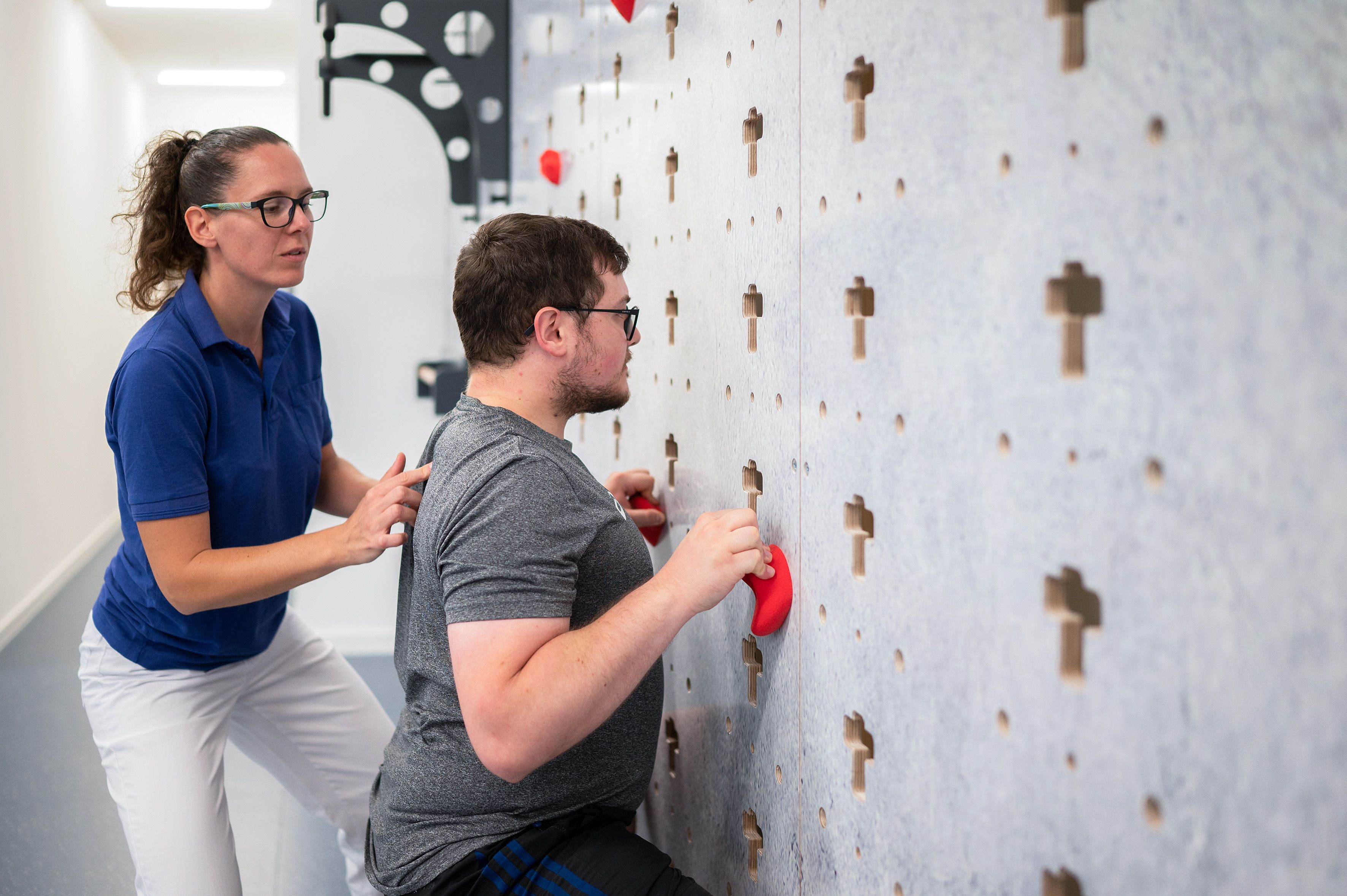 Eine Trainerin korrigiert die Körperhaltung eines jungen Mannes an der Kletterwand.