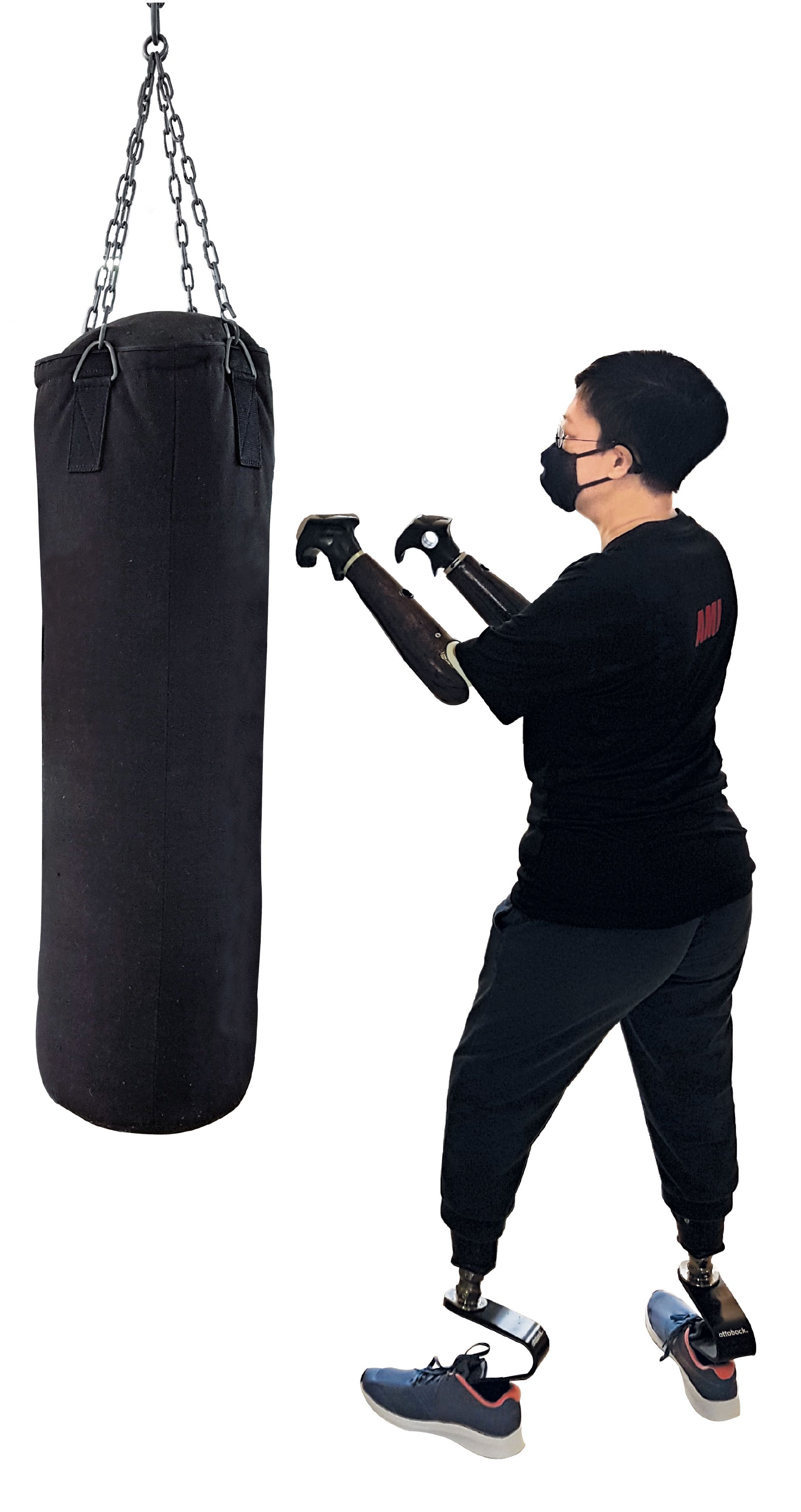Junge Frau mit Arm- und Beinprothesen trainiert an einem großen Boxsack. Sie trägt eine FFP2-Maske.