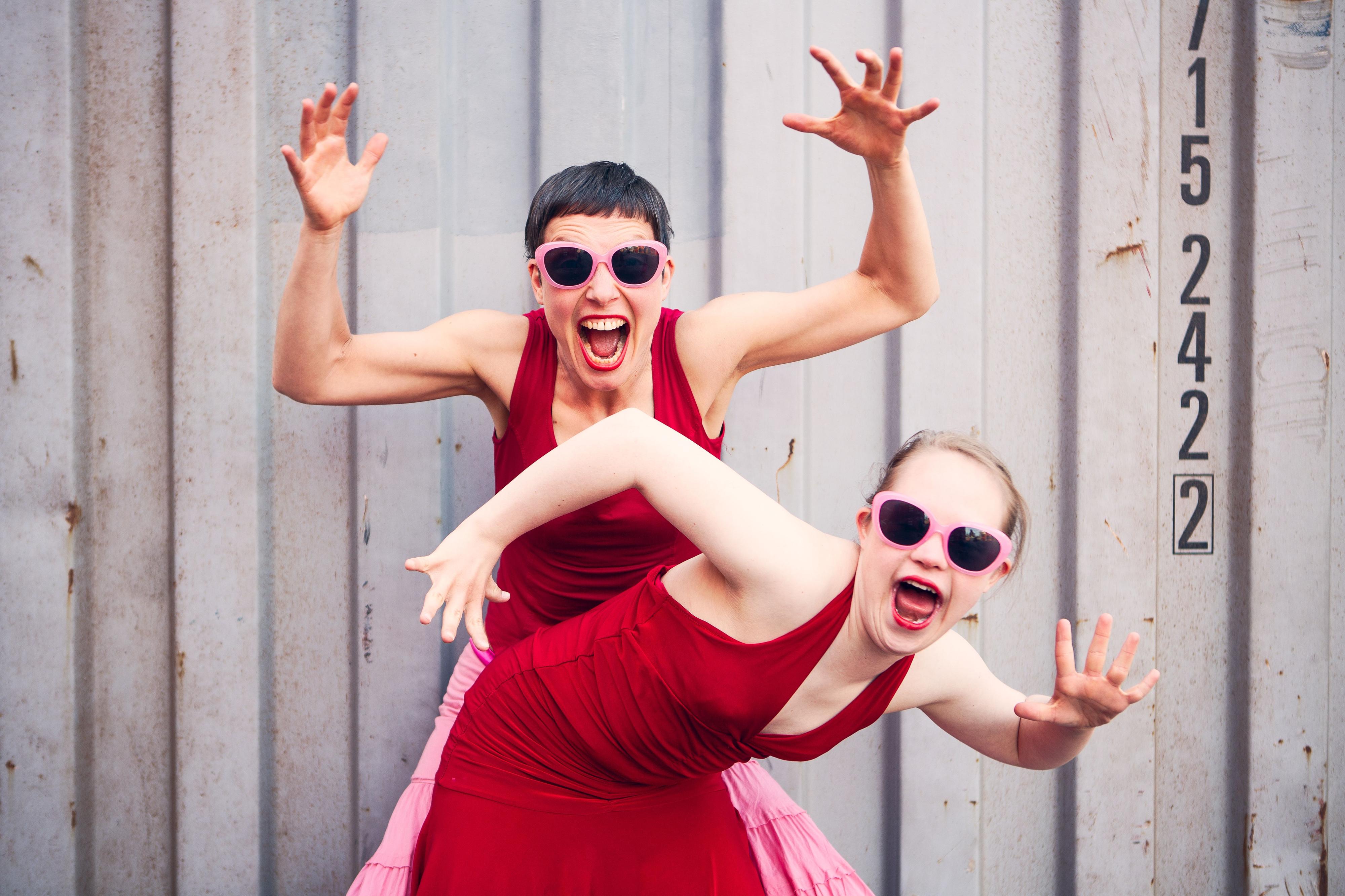 Zwei Tänzerinnen tanzen in roten Kleidern vor einem Schiffscontainer.