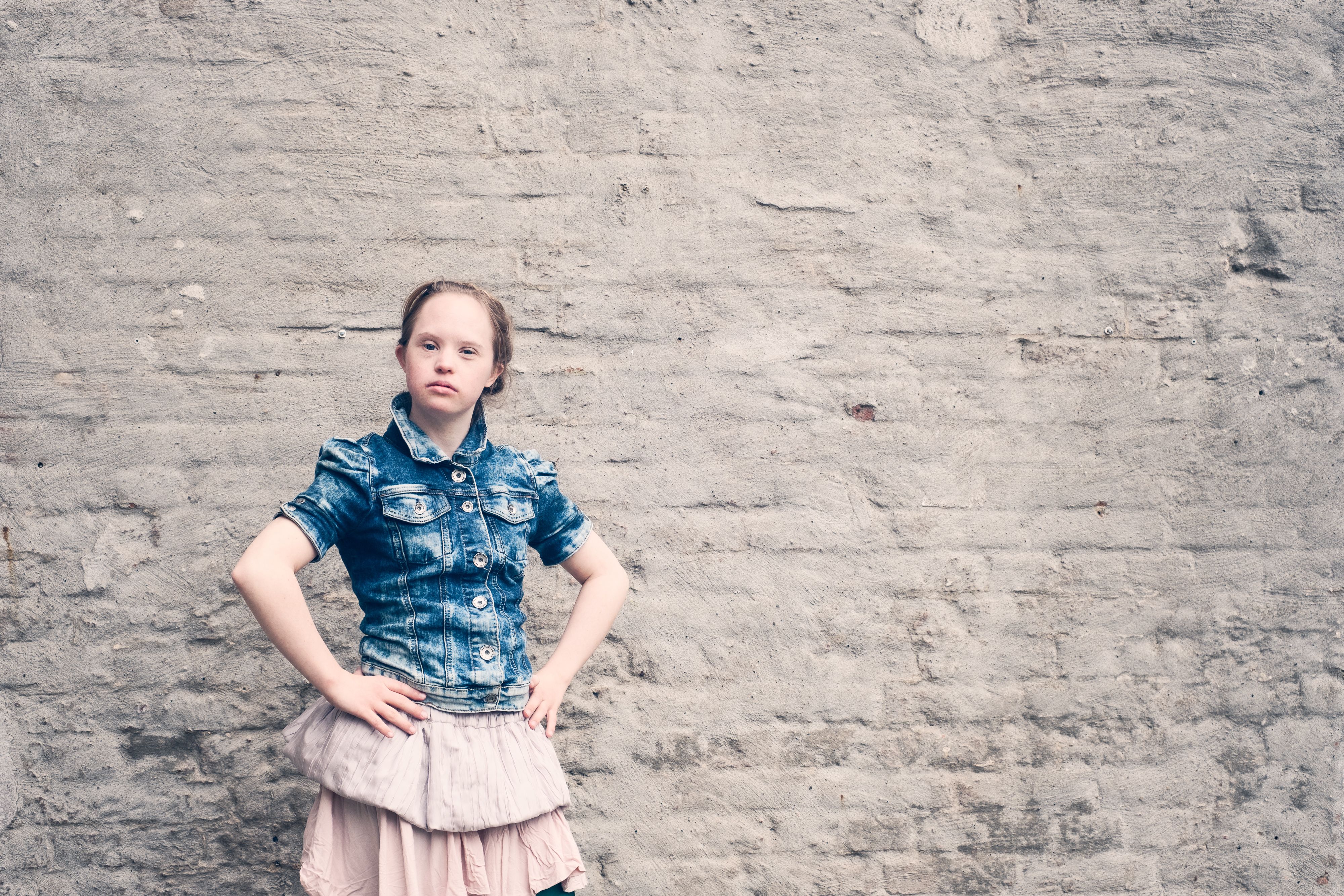 Ein junges Mädchen in Rock und Jeansjacke vor einer alten Hauswand.