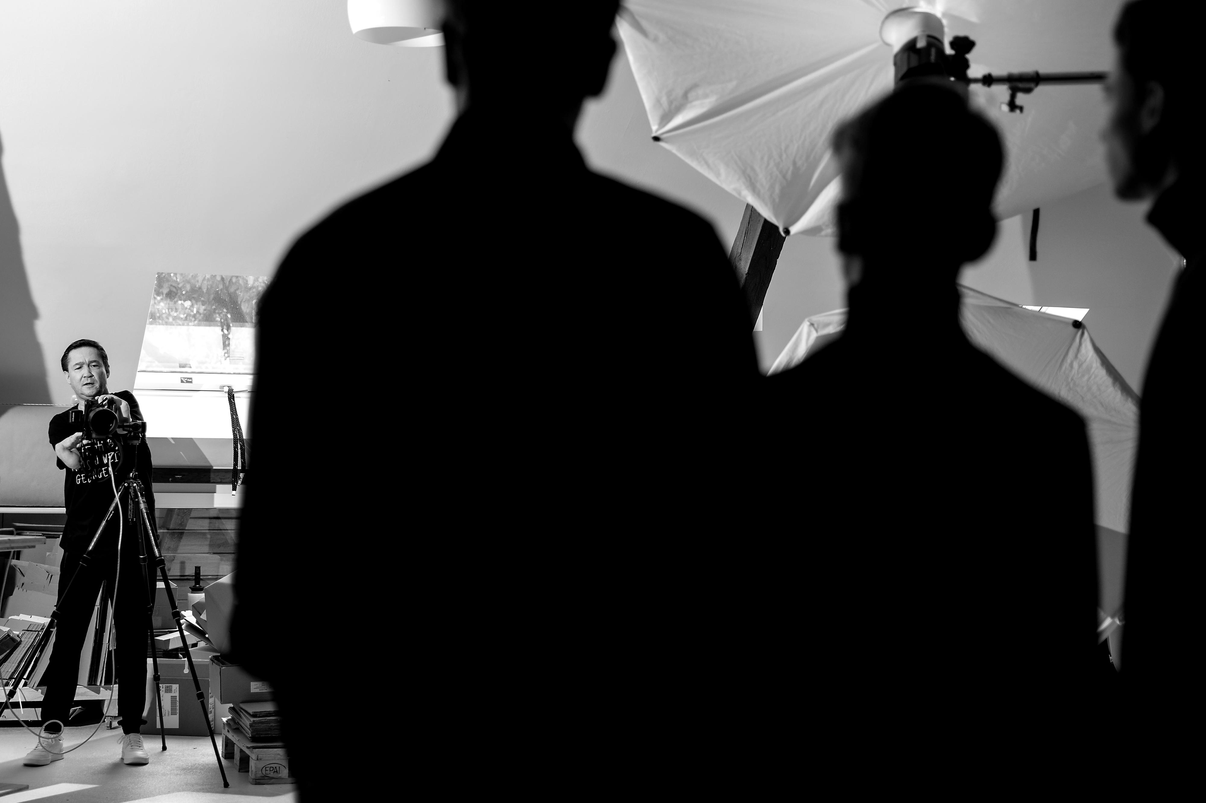 Ein contergangeschädigter Fotograf bei der Arbeit in einem Atelier. Im Vordergrund stehen drei Personen von der Kamera abgewandt.