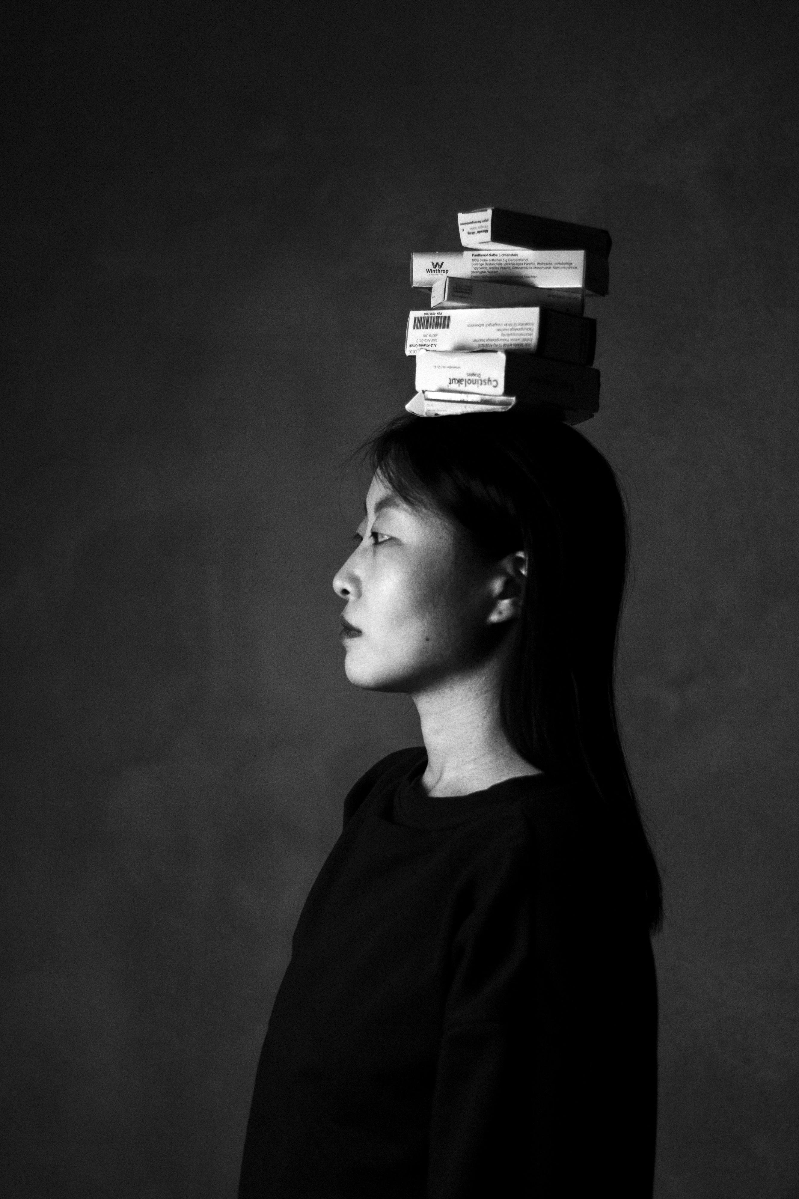 Porträt einer Frau im Profil - sie trägt Medikamentenschachteln auf den Kopf.