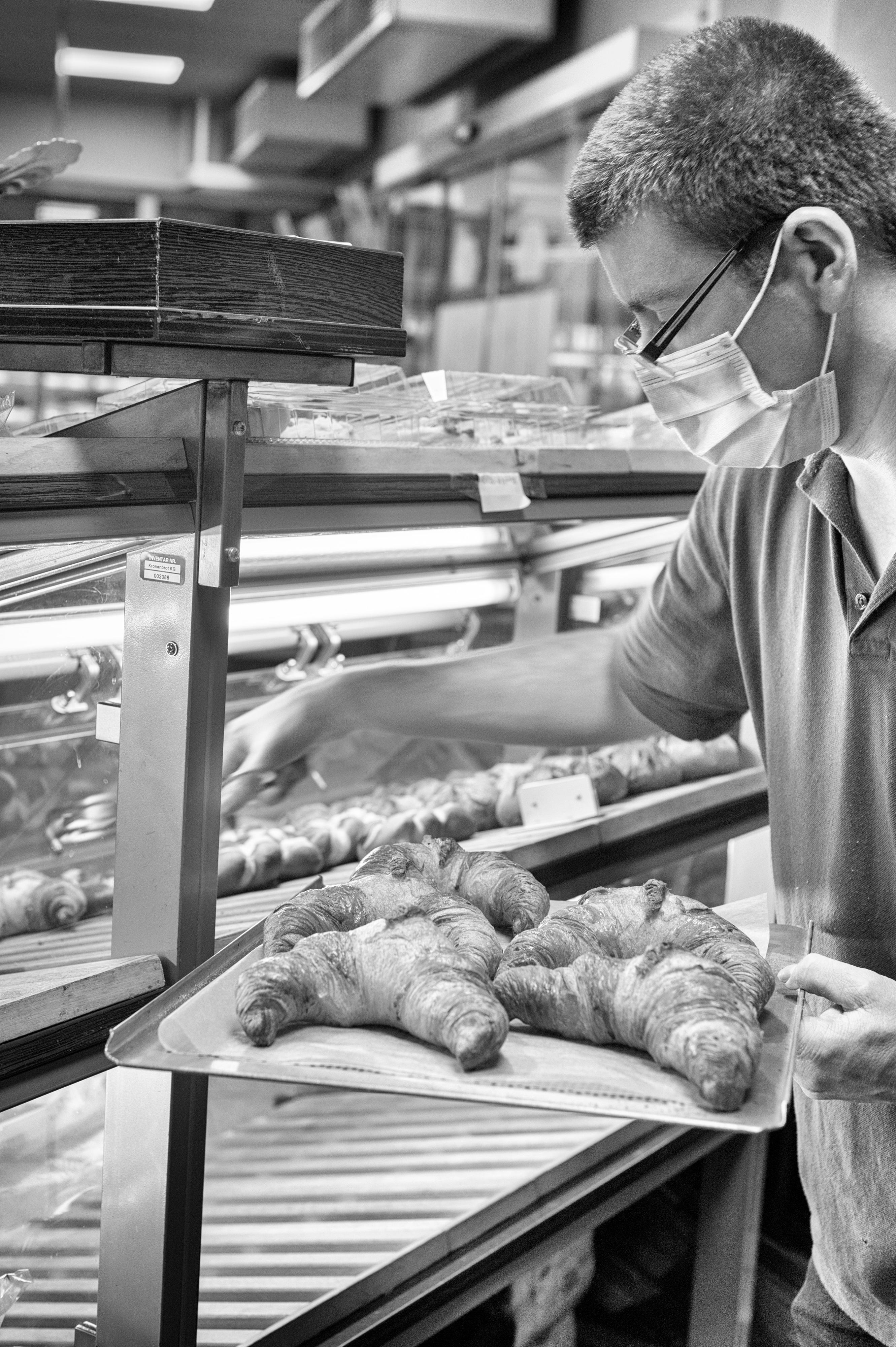 Ein junger Mann mit Mundschutz legt Croissants in einen Verkaufstresen.