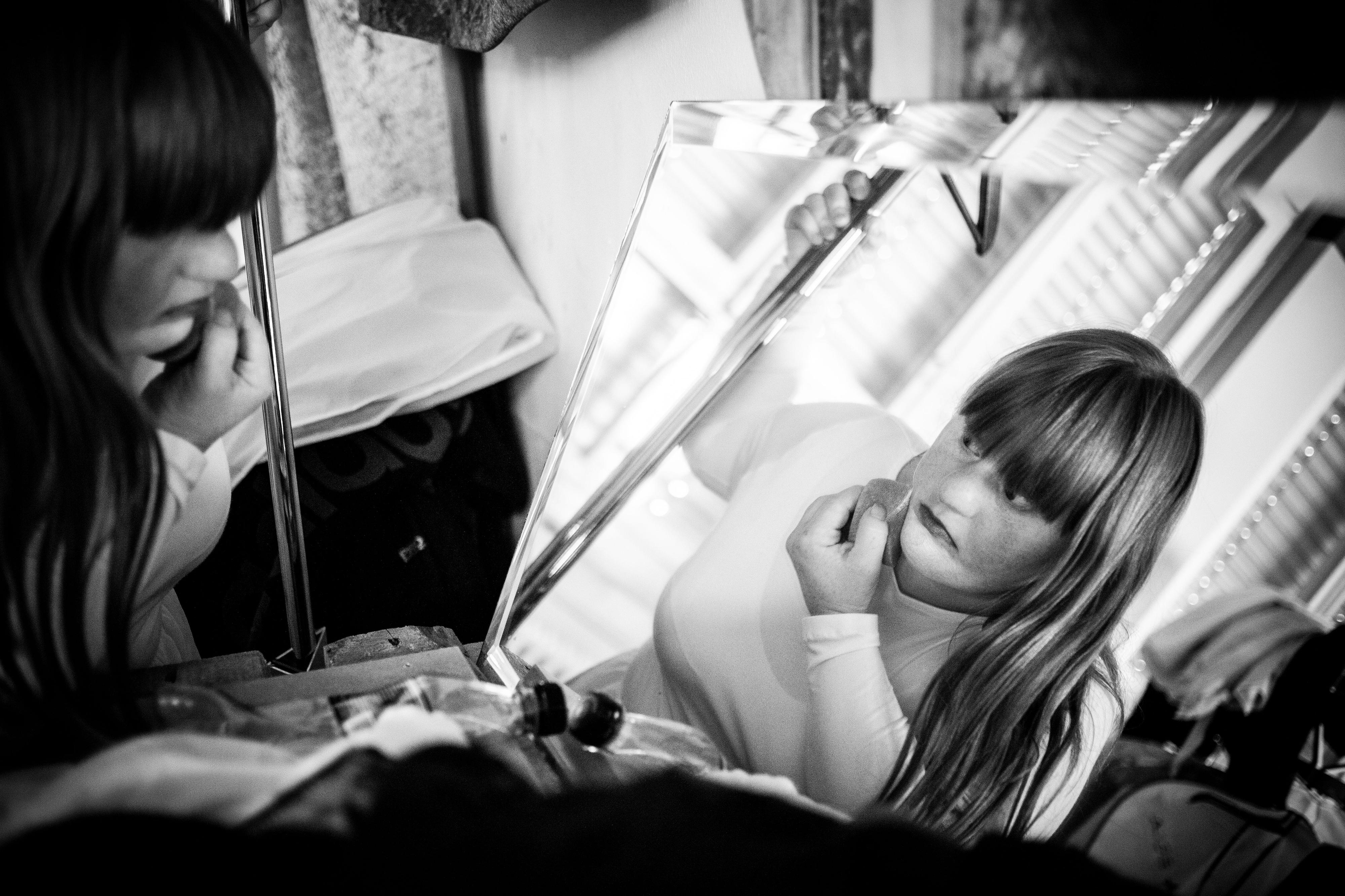 Eine junge Frau sitzt vor einem Spiegel und schminkt sich.