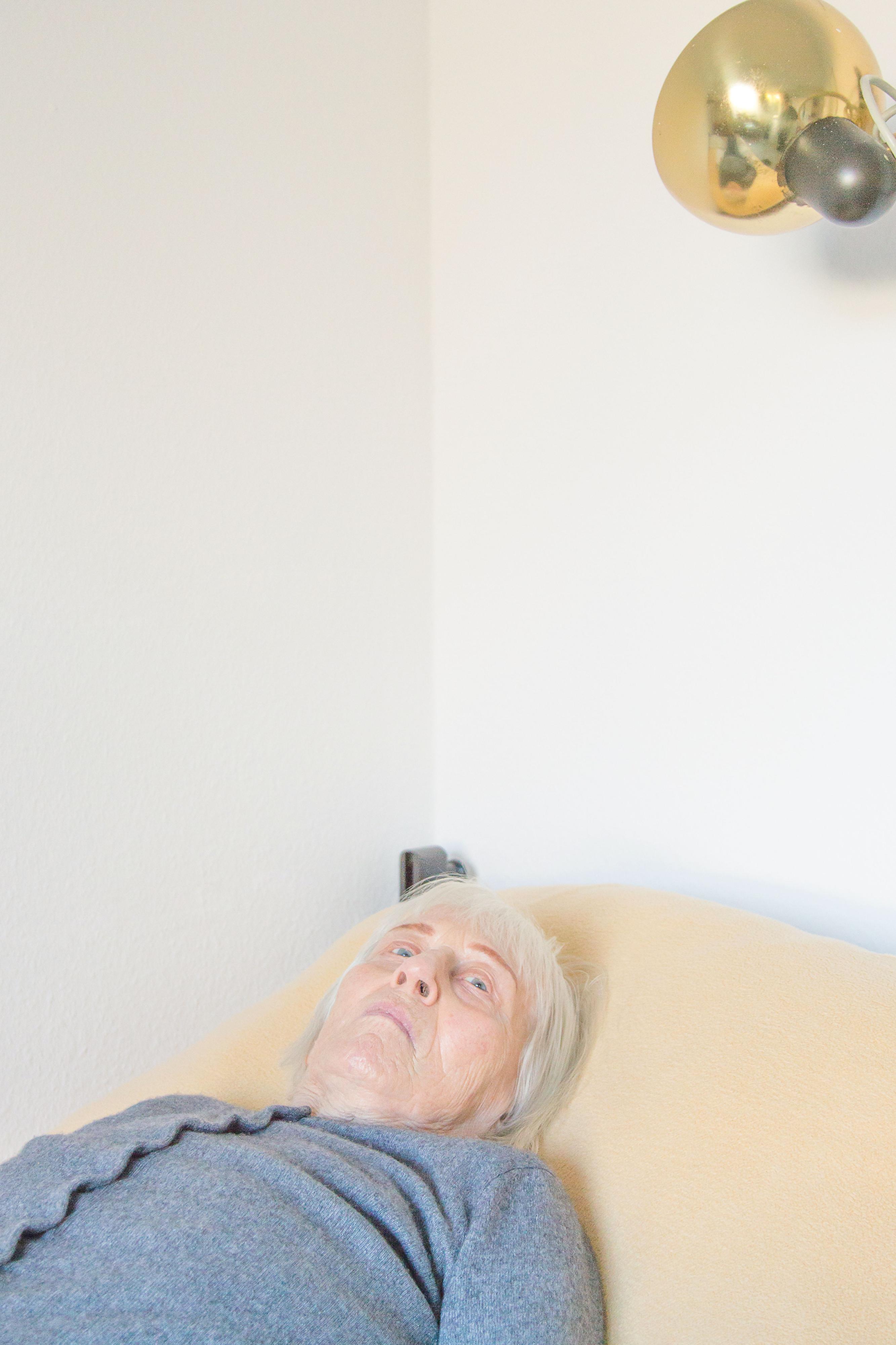 Eine ältere Frau liegt auf einem Bett und schaut an die Decke.