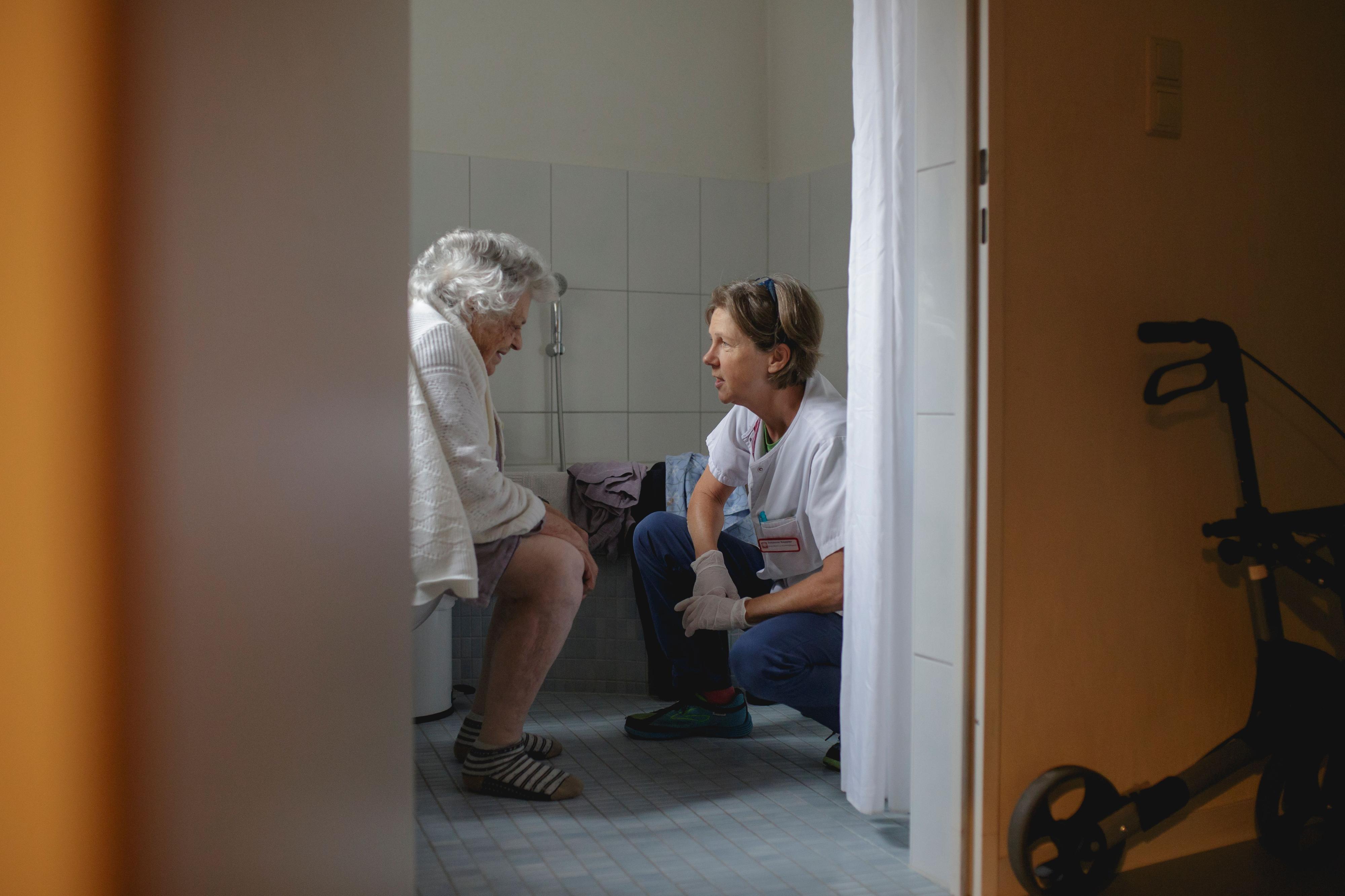 Eine Patientin sitzt auf der Toilette. Eine Pflegerin kniet ihr gegenüber.