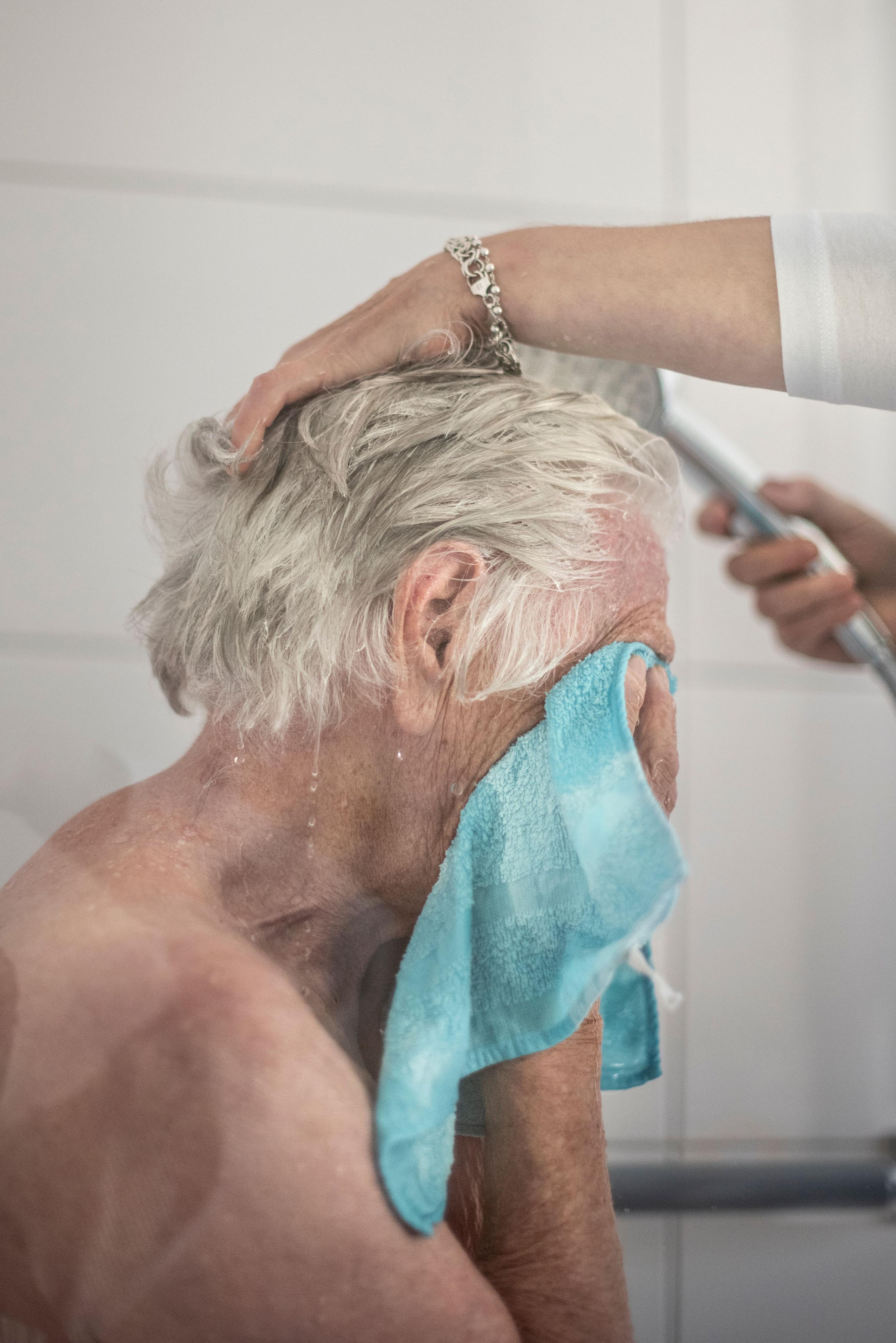 Ein älterer Mann hält sich ein Handtuch vor das Gesicht, während seine Haare gewaschen werden.