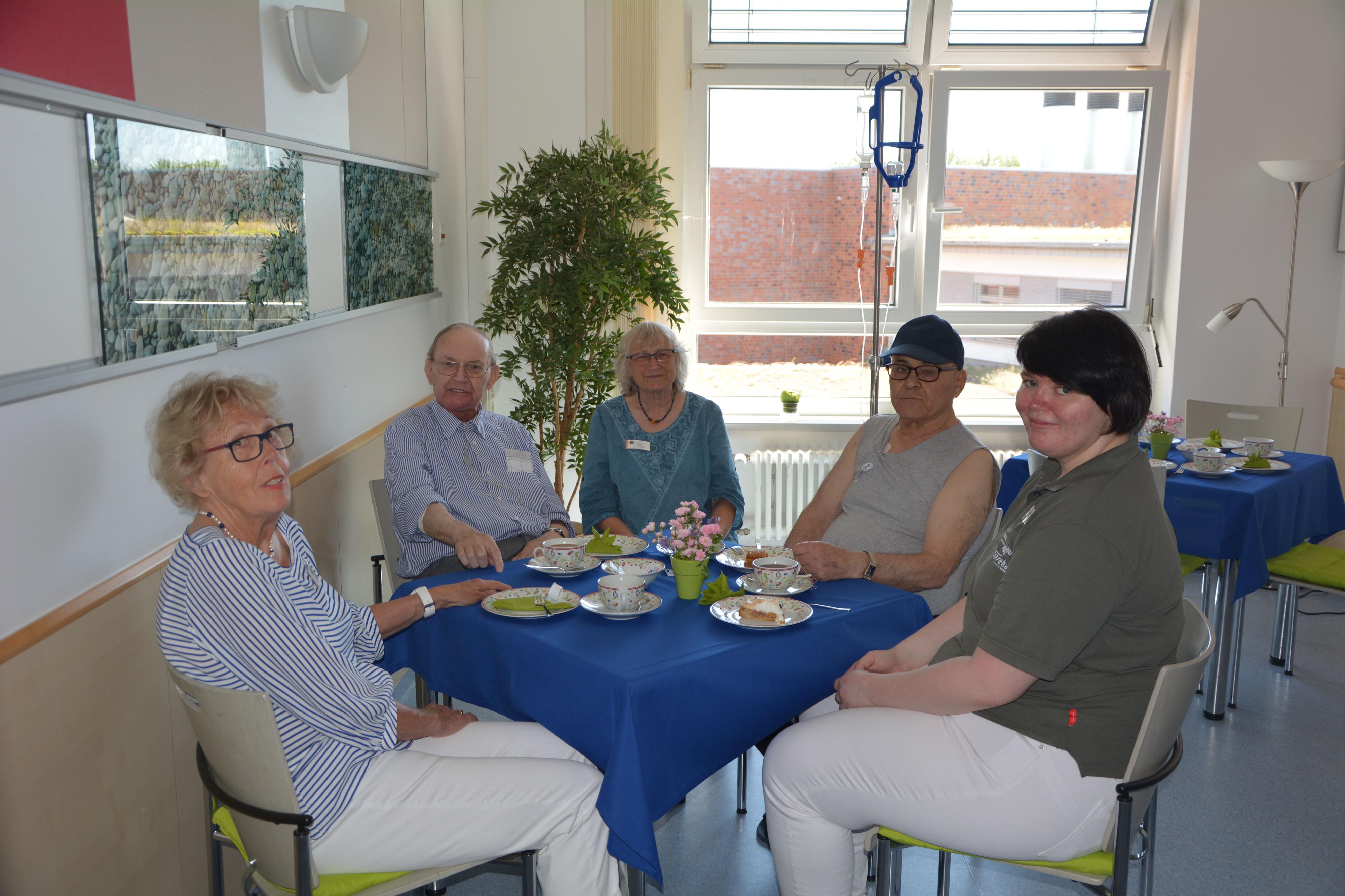 Fünf Personen sitzen um einen Tisch mit Kaffee und Kuchen.