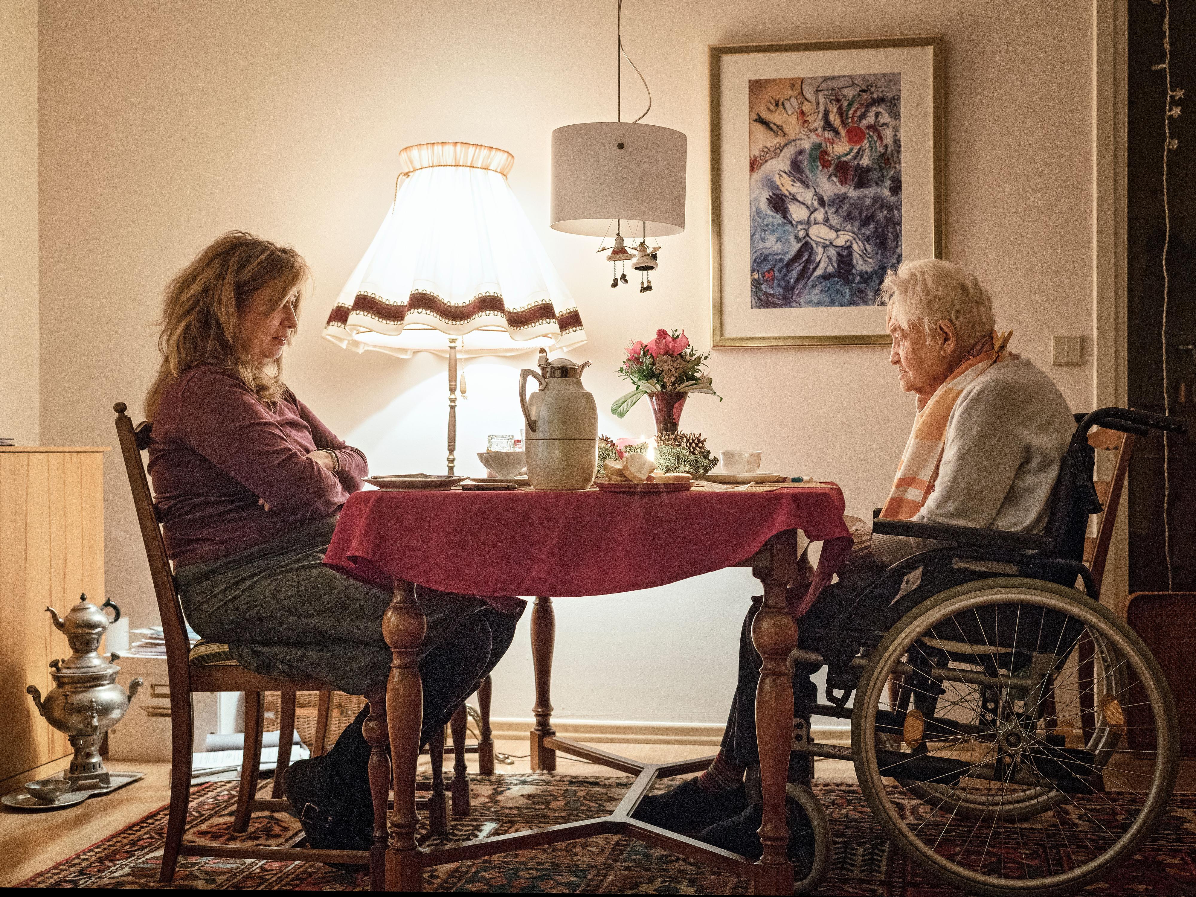 Eine ältere Frau im Rollstuhl sitzte mit einer jüngeren Frau an einem gedeckten Tisch.