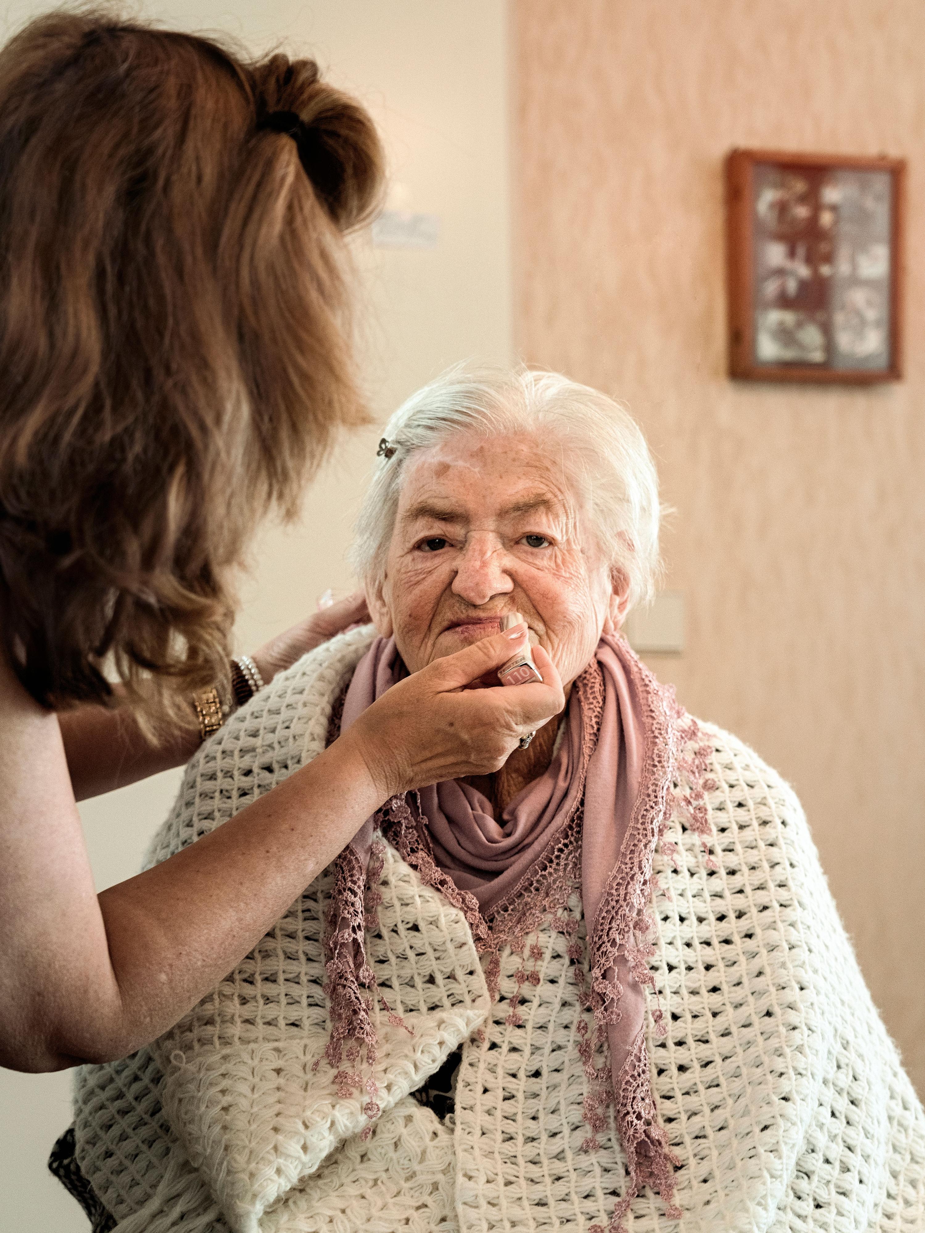 Eine Frau trägt einer älteren Frau Lippenstift auf.