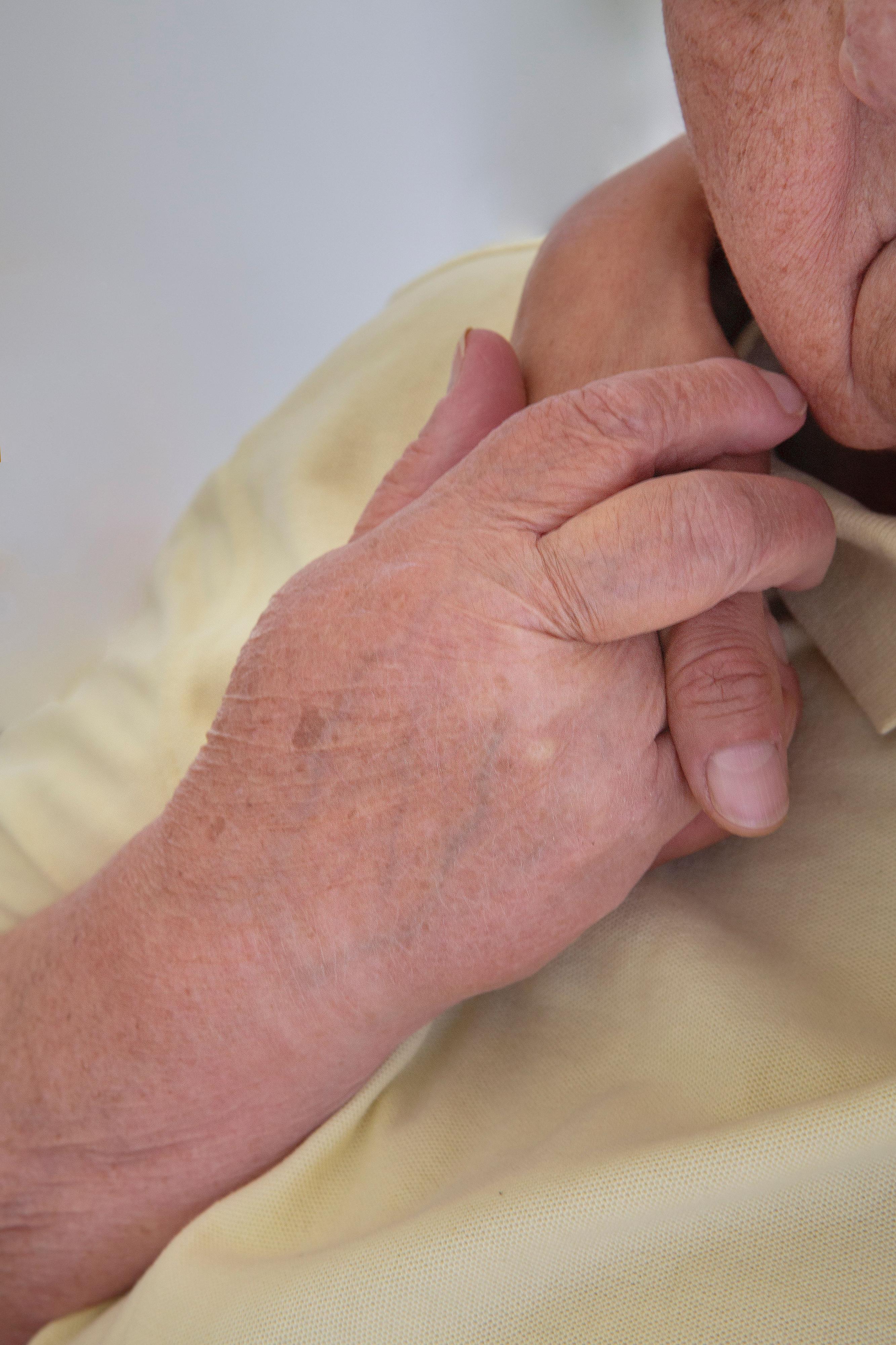 Eine ältere Person hält die Hand einer jüngeren, die um ihre Schulter liegt.