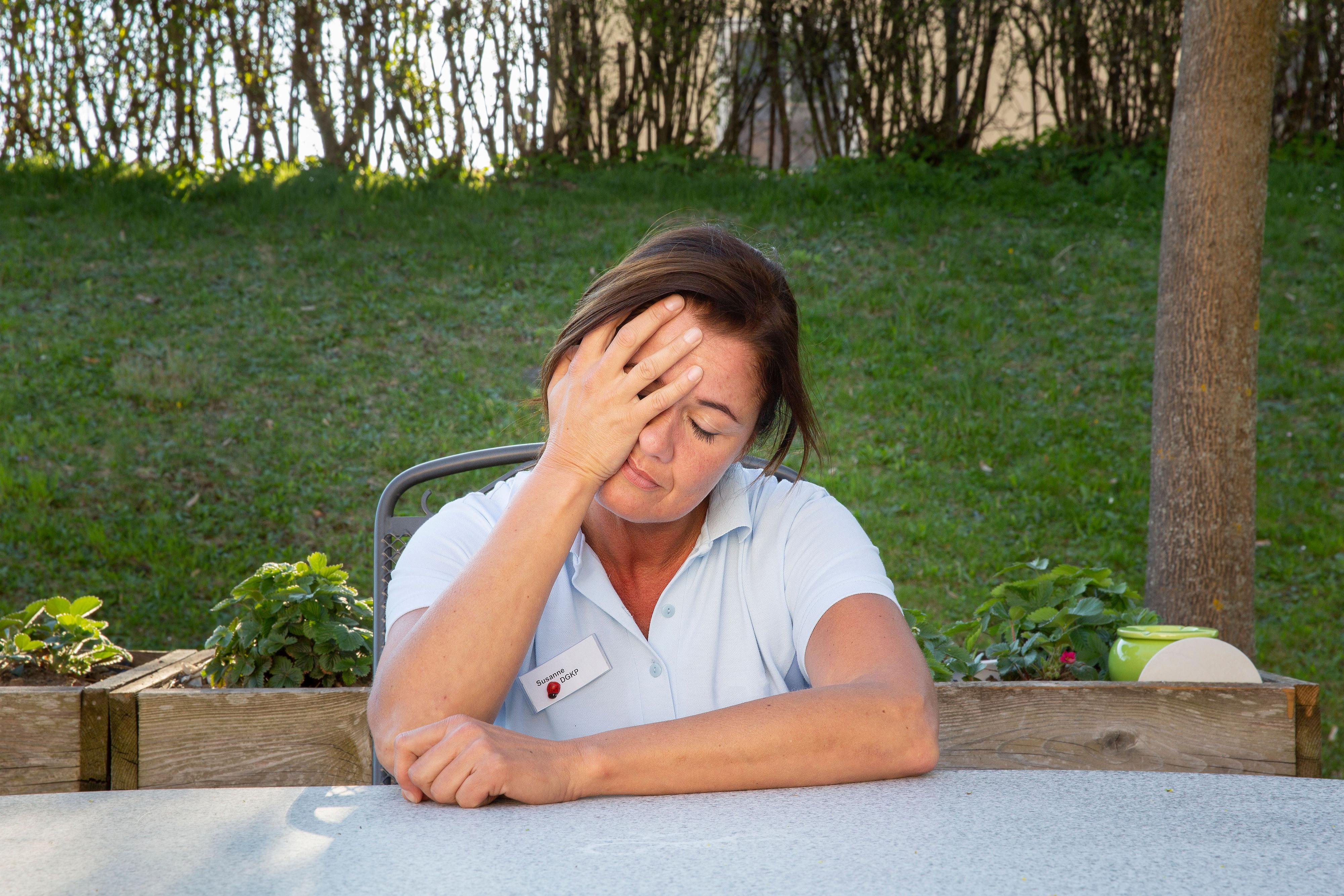 Eine Pflegerin sitzt erschöpft an einem Tisch in einem Garten.