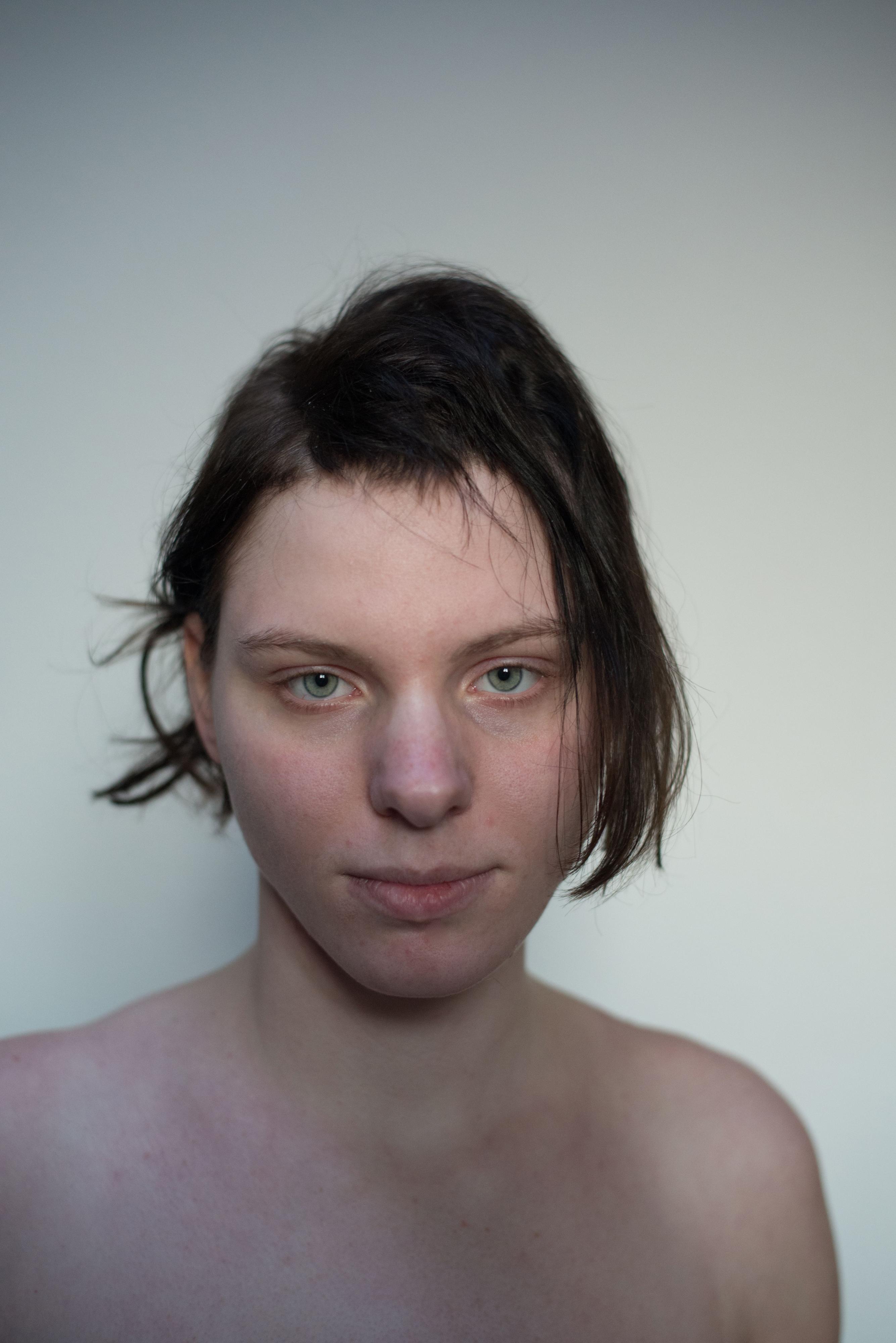 Eine junge Frau mit unregelmäßig geschnittenem Haar im Porträt bis zu den nackten Schultern.