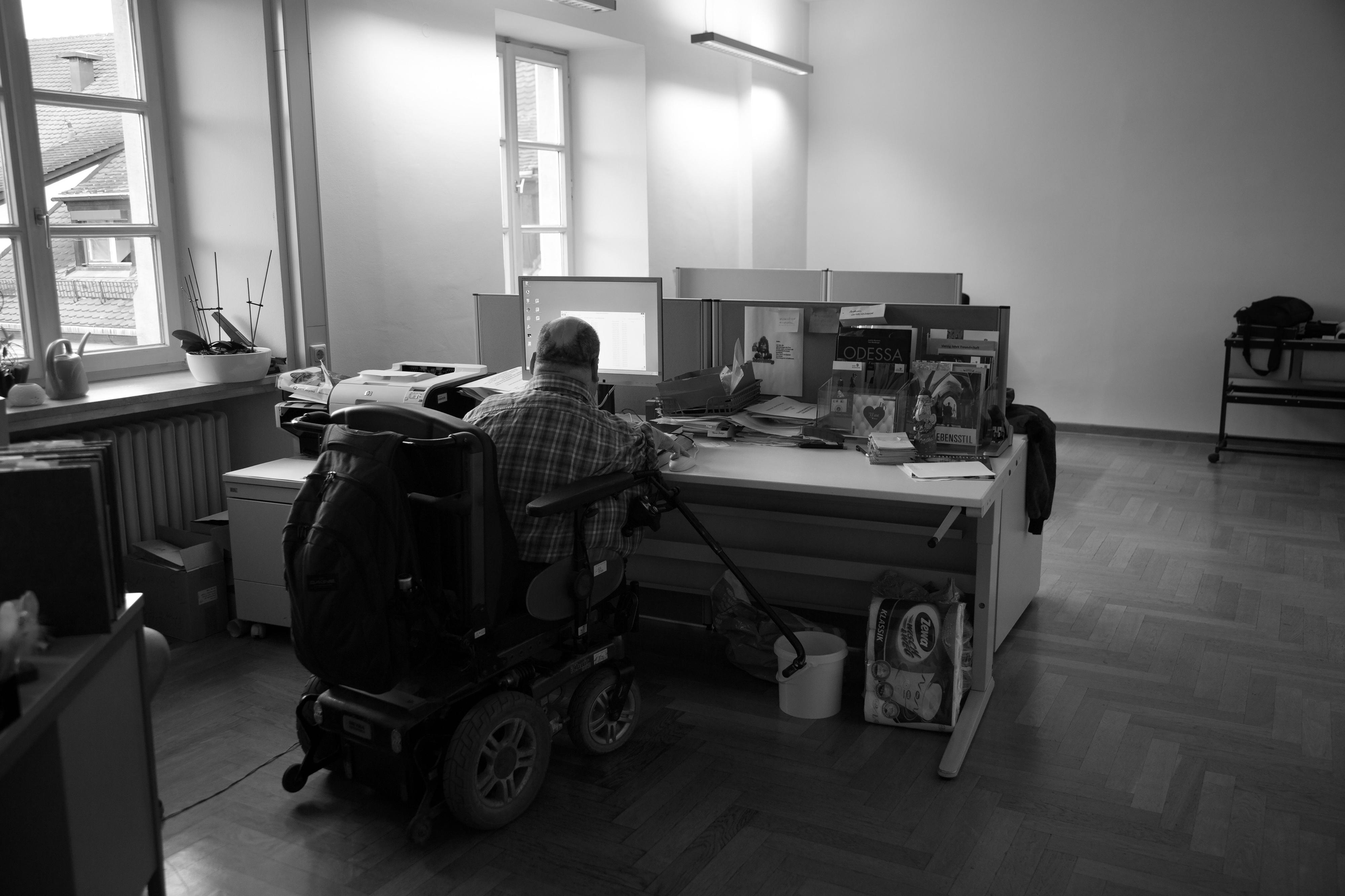 Ein Mann im Rollstuhl sitzt an einem Schreibtisch und arbeitet.
