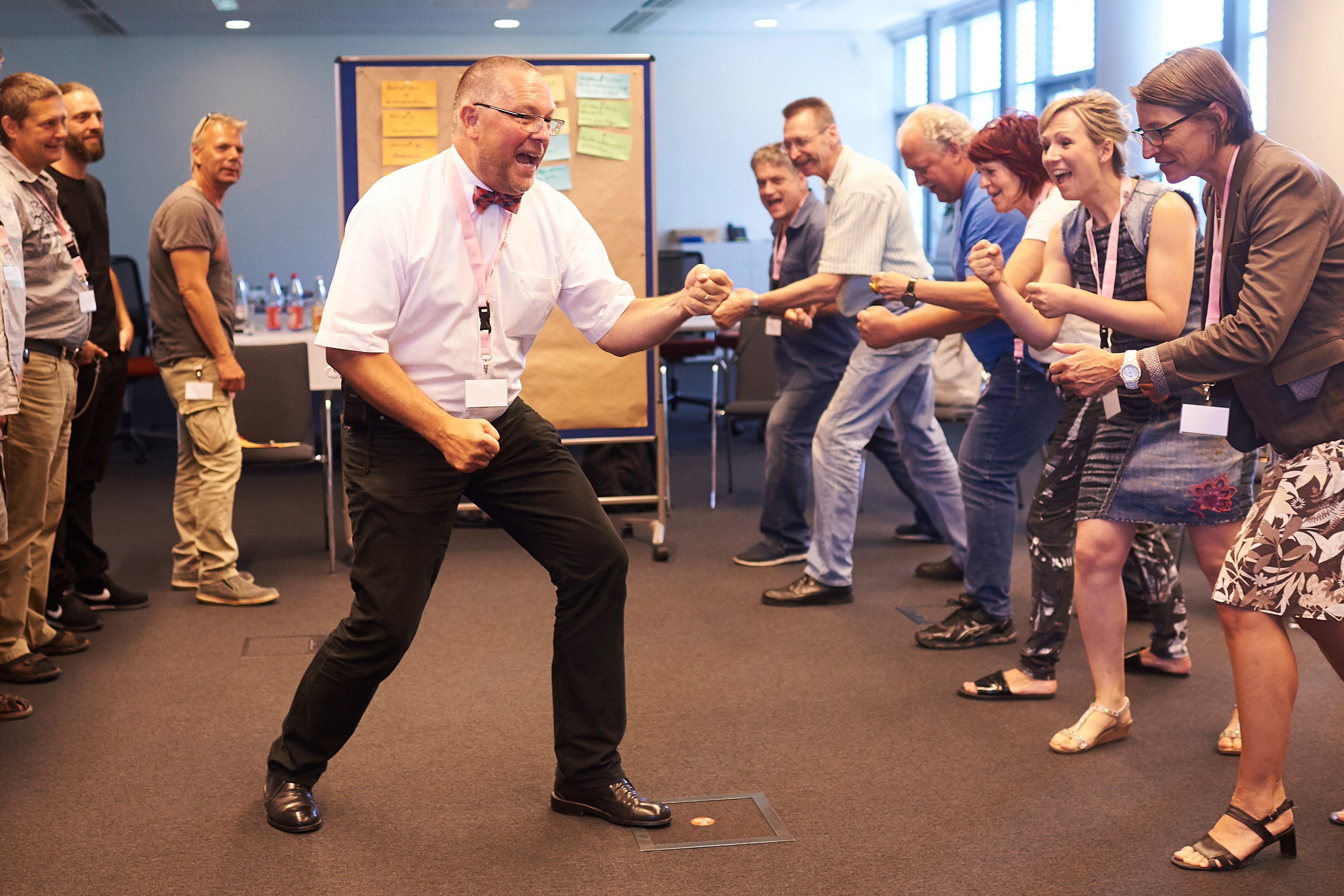 Workshop-Leiter steht vor einer Personen-Gruppe und macht eine Box-Bewegung - alle aus der Personengruppe machen die gleiche Bewegung. Alle rufen etwas.