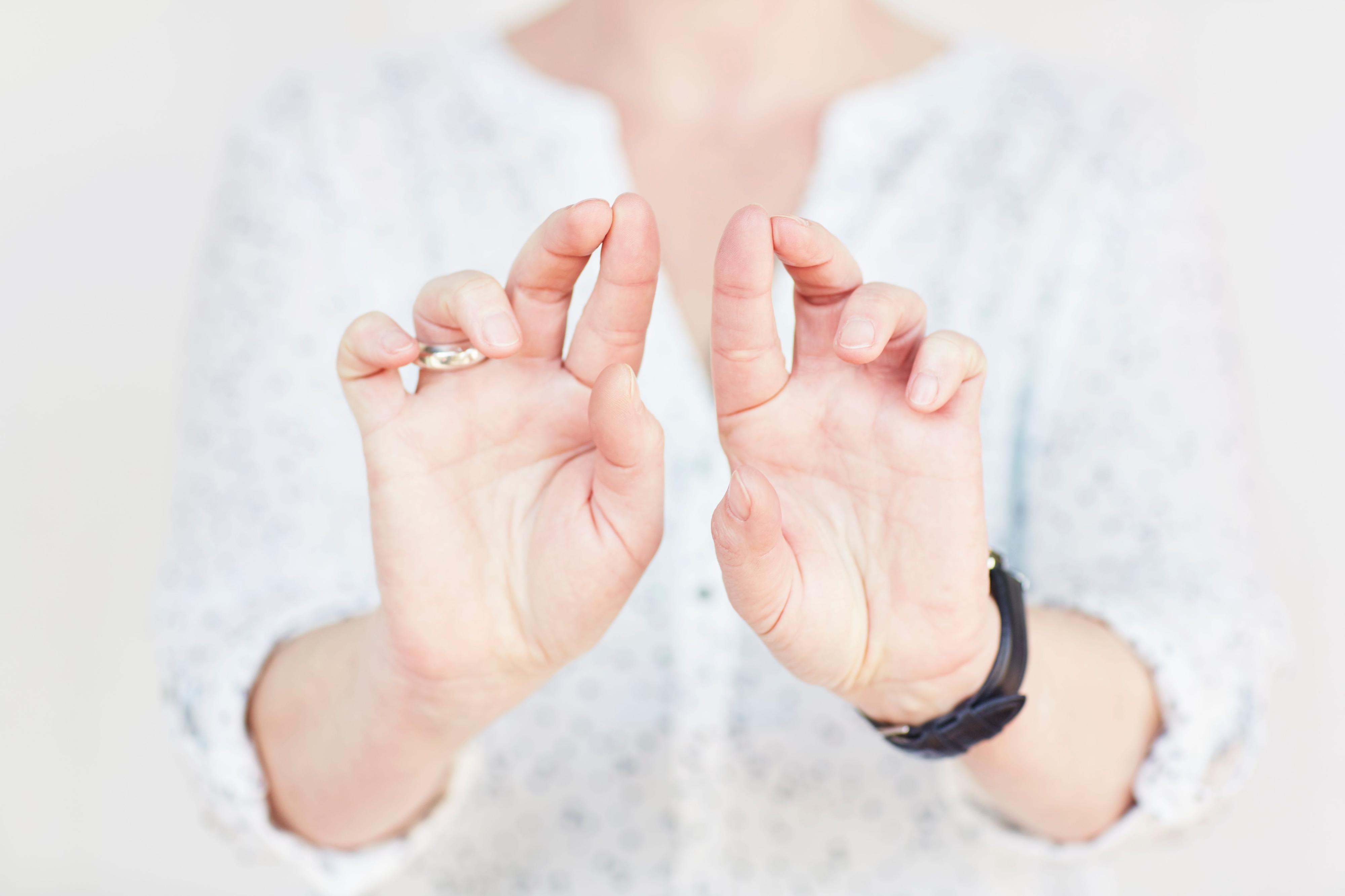 Die Hände einer Frau. Die Handinnenflächen sind der Kamera zugewandt, Zeige- und Mittelfinger jeder Hand sind nach oben gerichtet und berühren sich an den Spitzen.