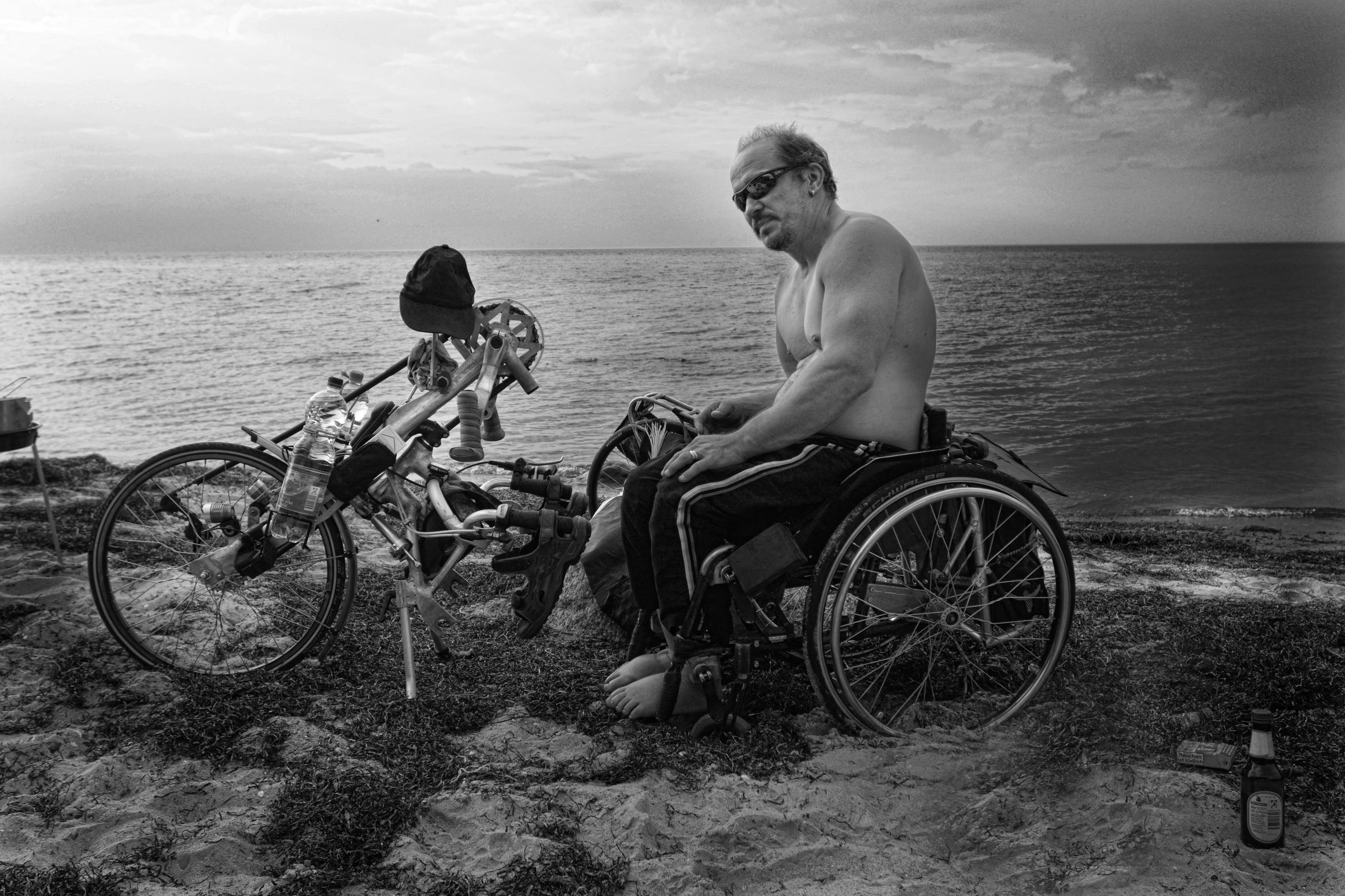 Ein Mann sitzt in einem Handybike am Meer.